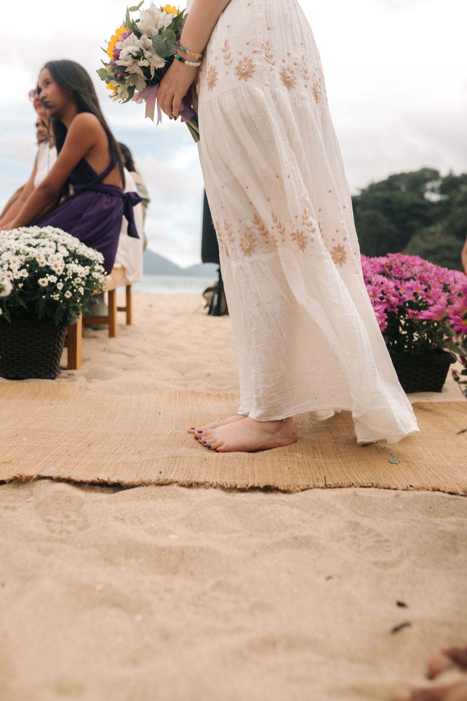 Barefoot on burlap runner with white wedding dress and pink flowers on a beach.