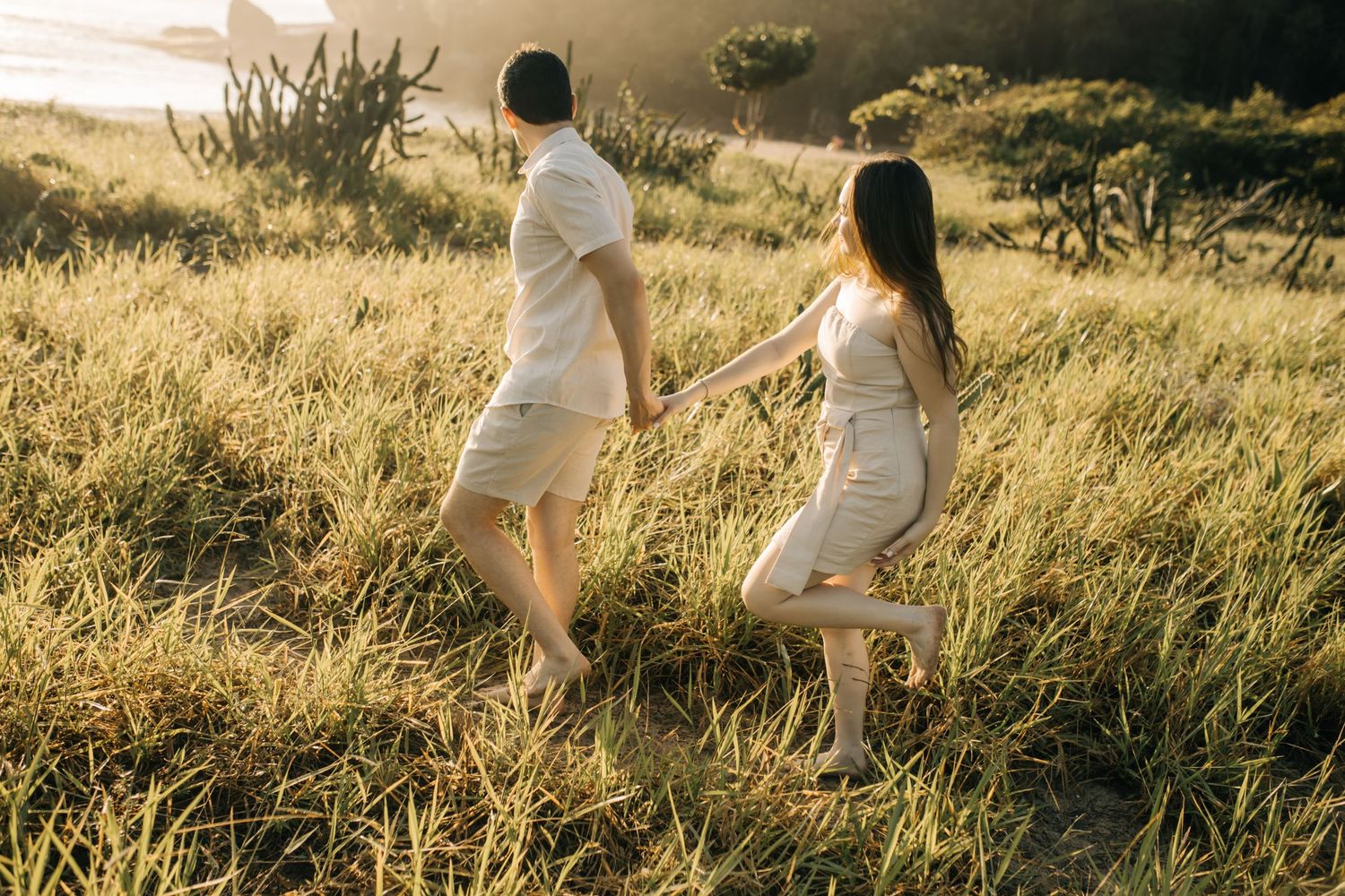 Couple walking uphill through golden grass during sunset.