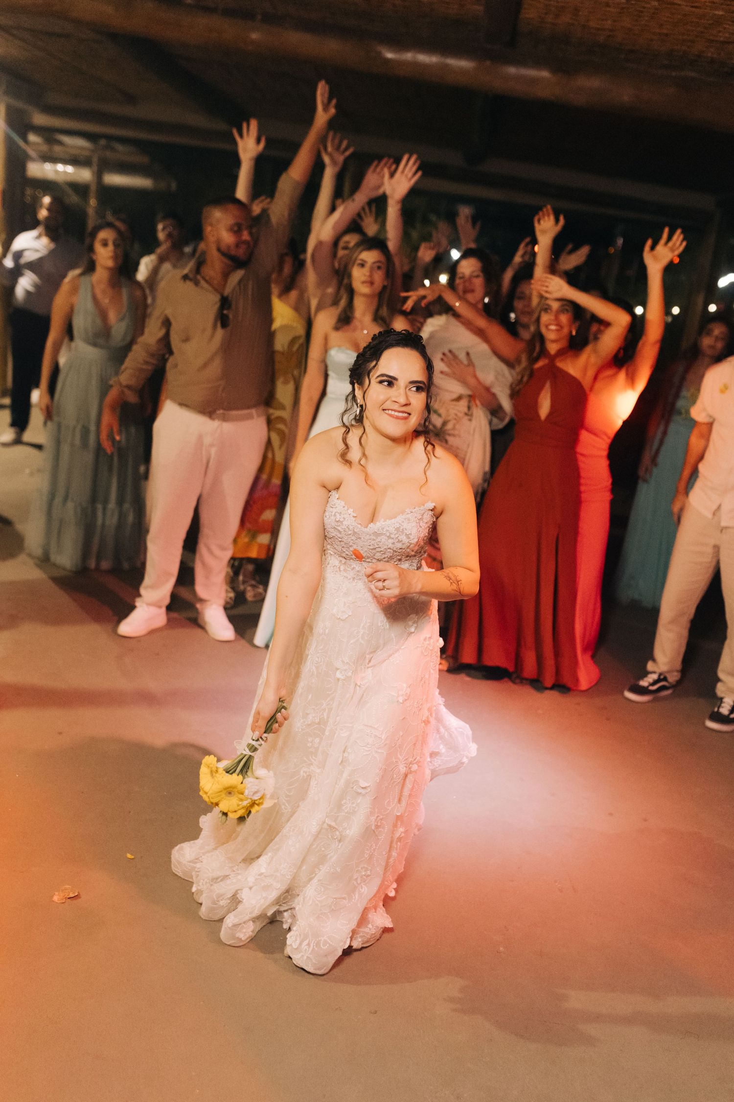 Bride holding bouquet during wedding reception with crowd cheering in background.