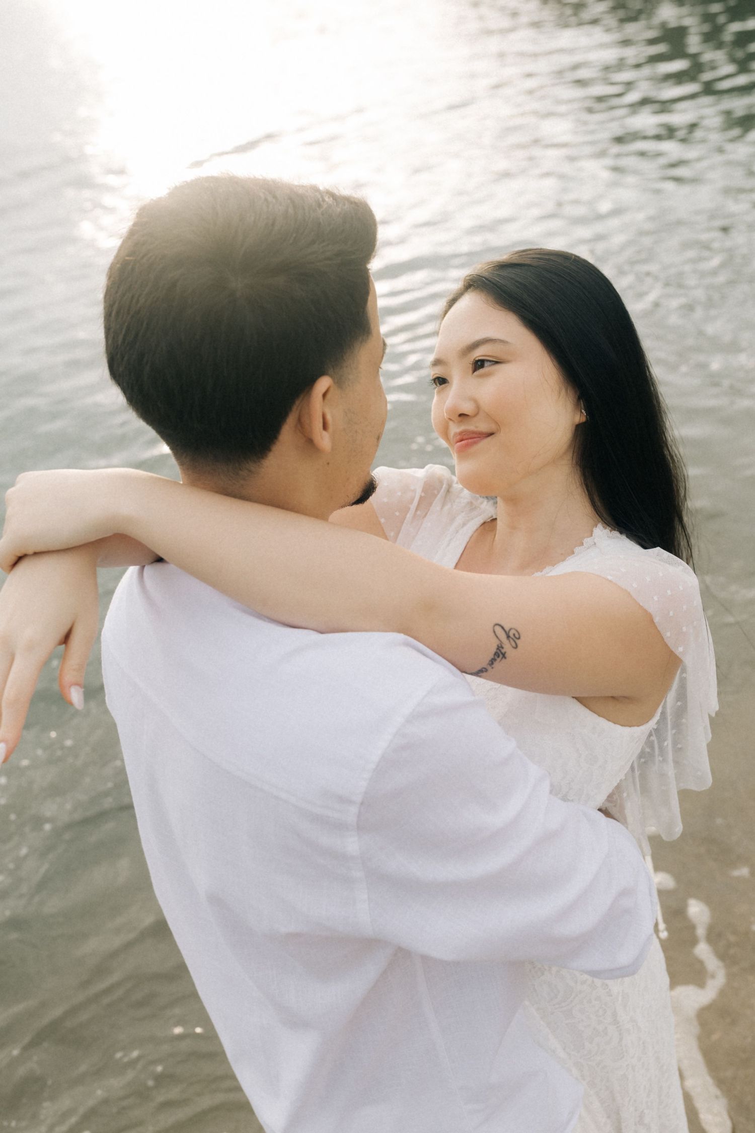 A couple embraces while standing in water during a seaside photoshoot.