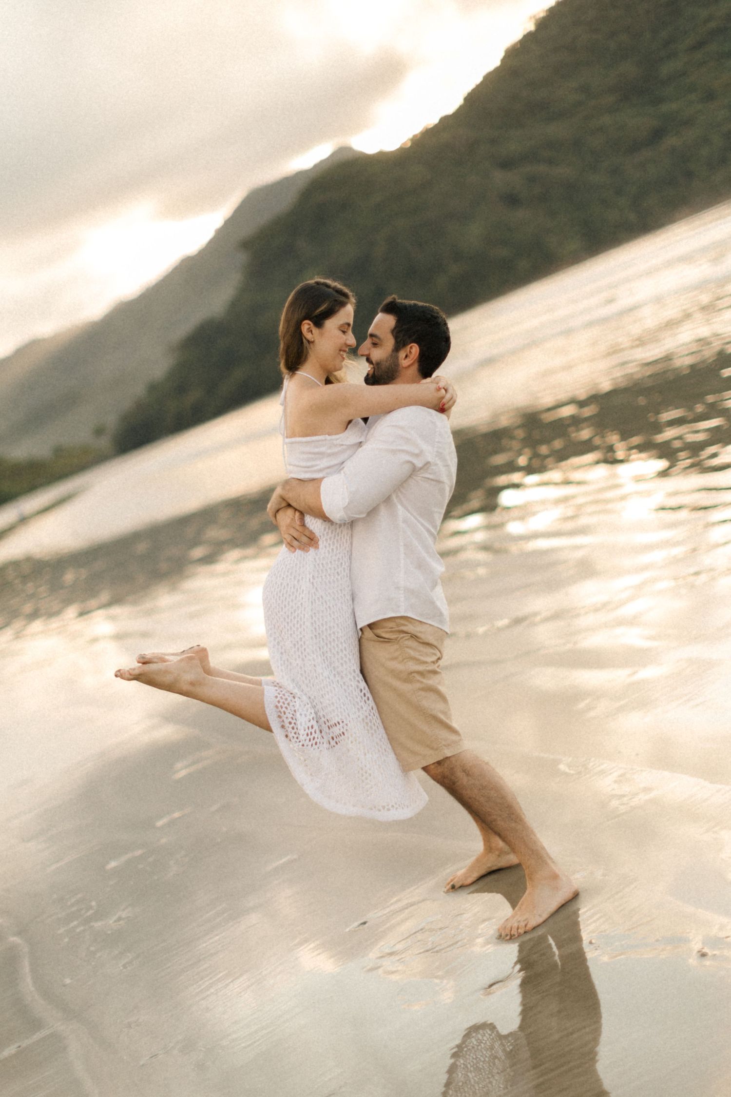A romantic beach photoshoot with playful lifting poses against a sunset backdrop.