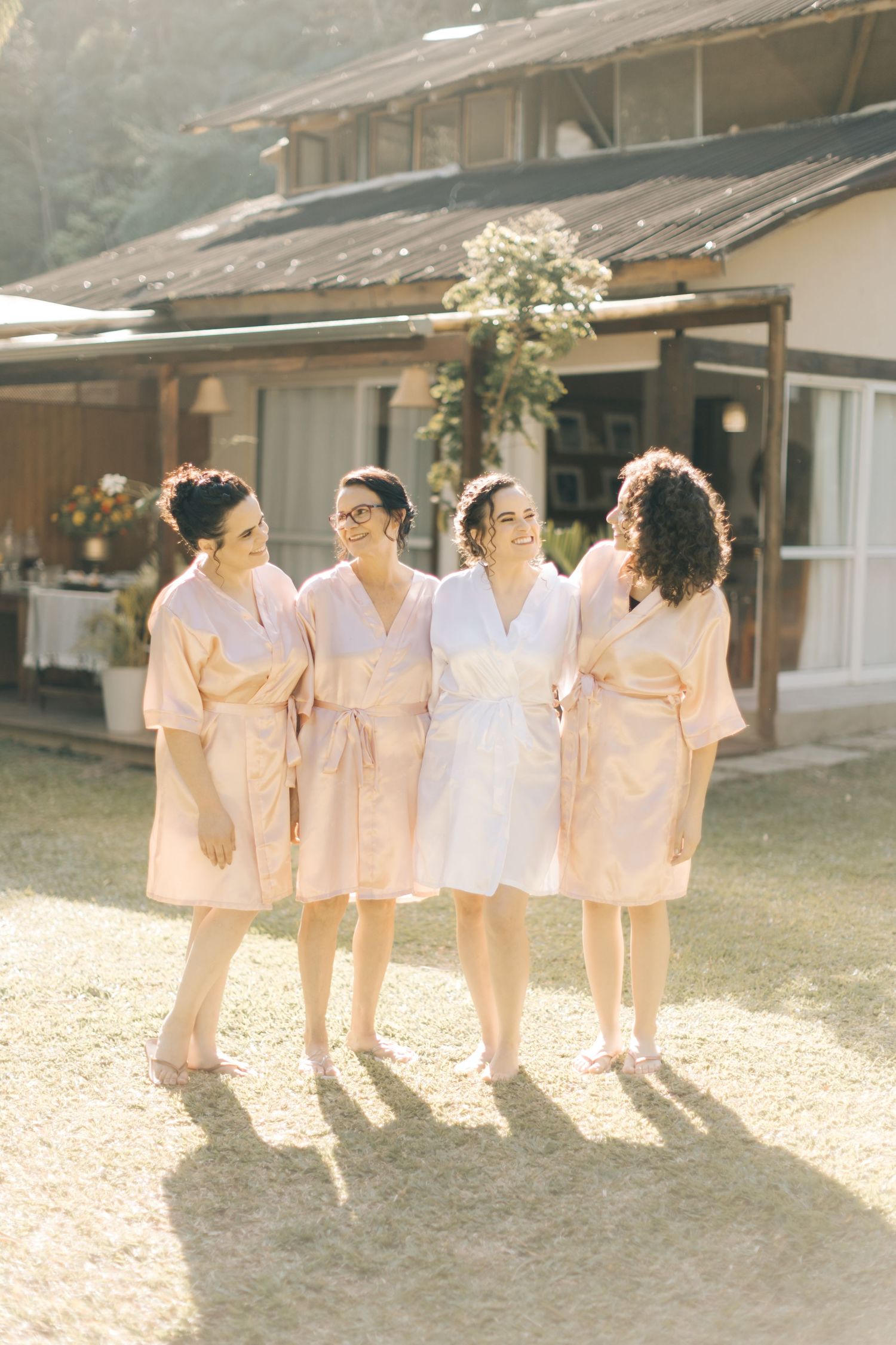 Bridesmaids in matching peach robes stand together outside a rustic venue.
