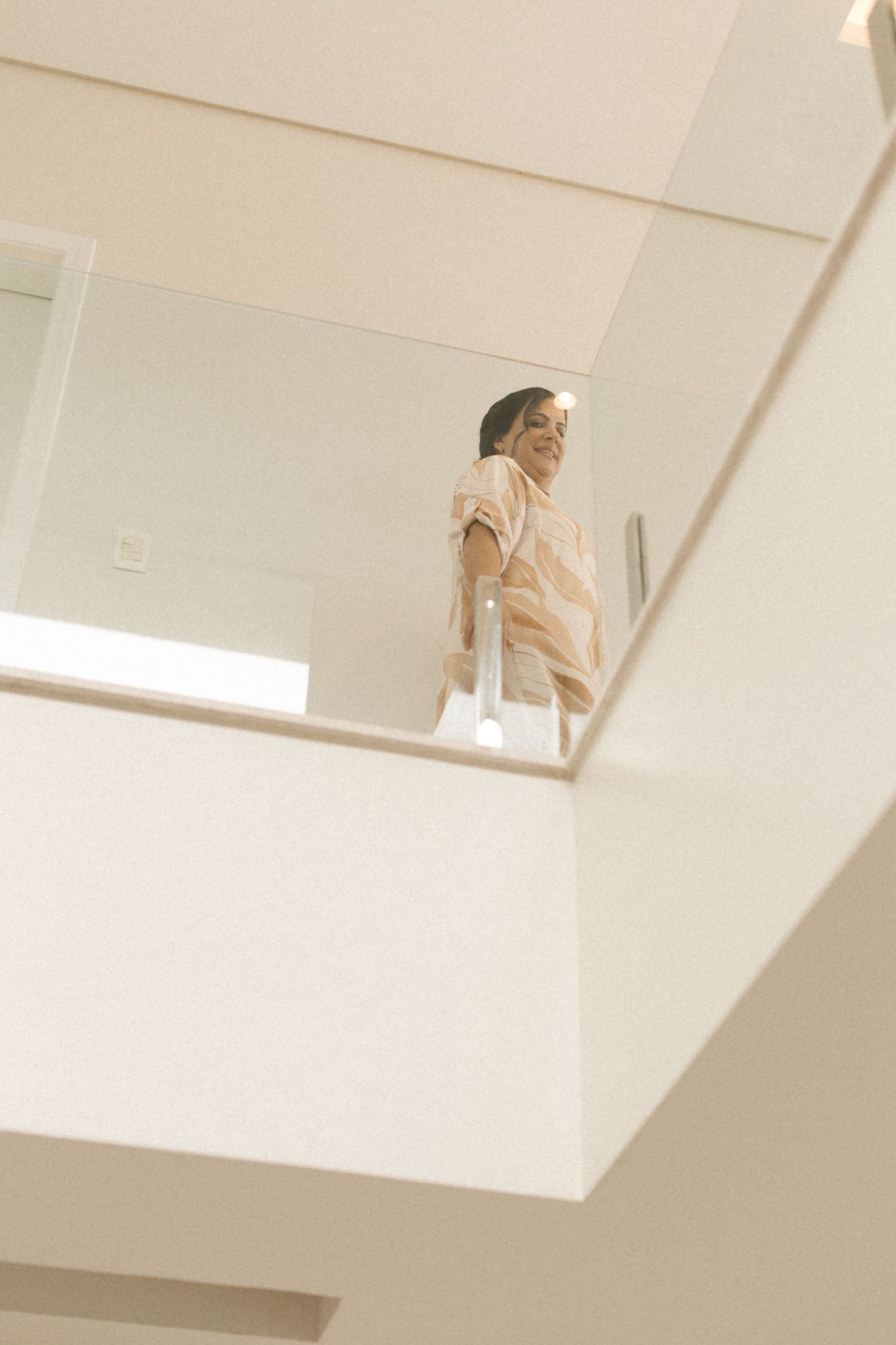 Figure in light clothing stands at edge of modern interior balcony or mezzanine.