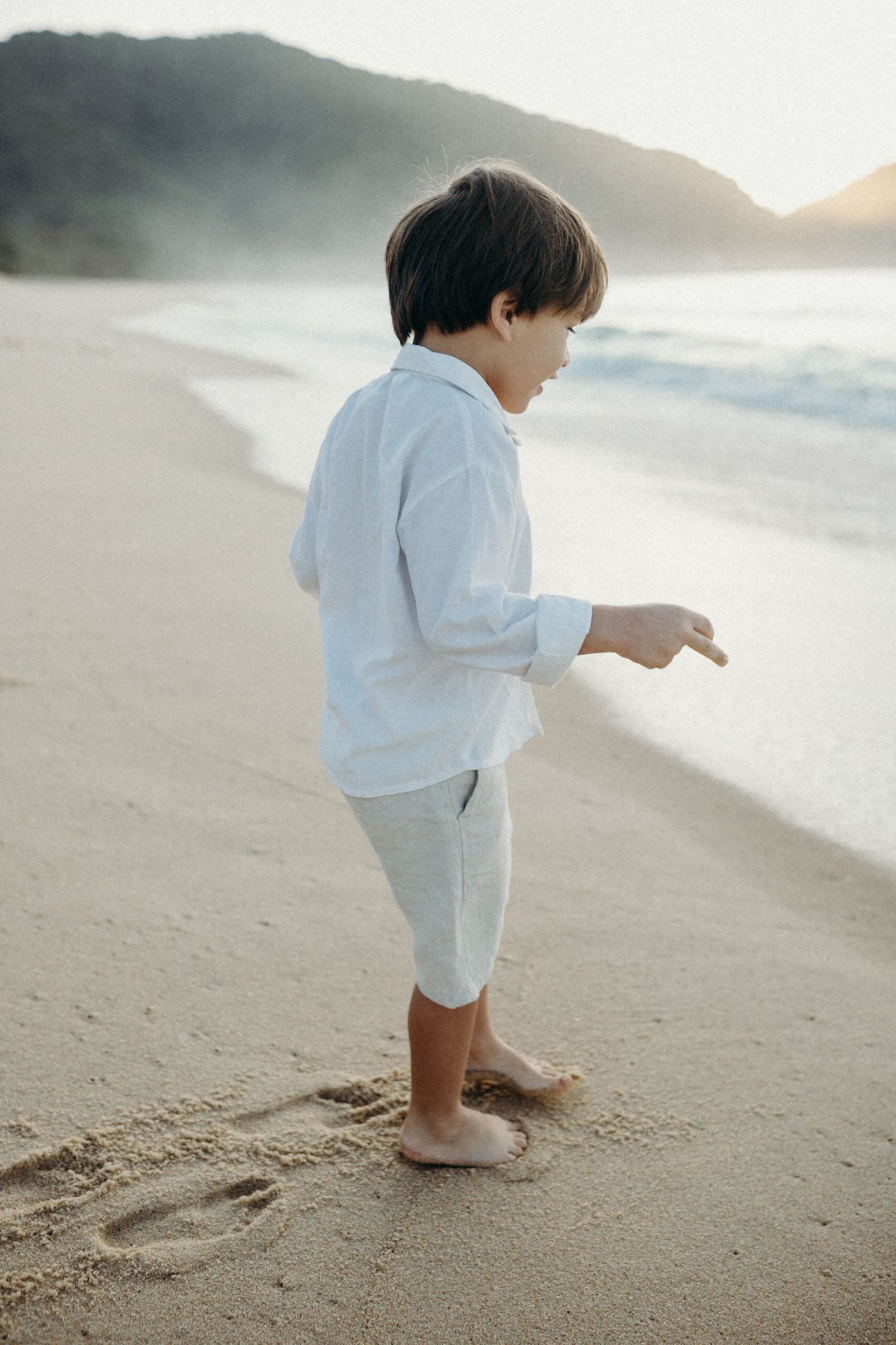 A small child in white clothing playing barefoot on a sandy beach.