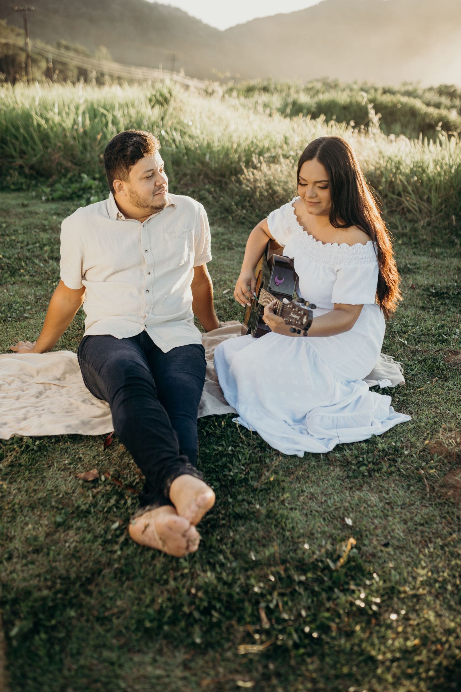 Couple relaxing on grass during sunset with mountains in background.