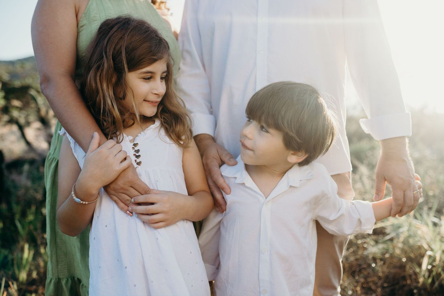 Two children share a playful moment outdoors with parents in the background.