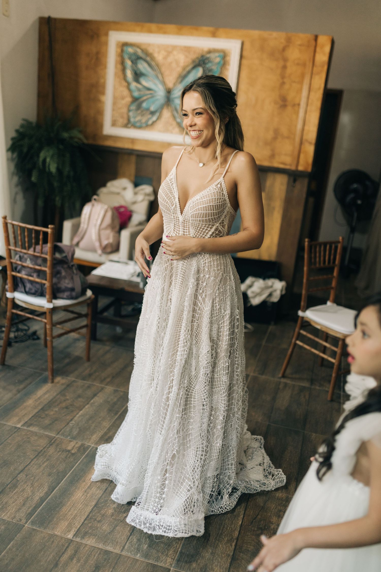 A detailed lace wedding gown is showcased in a room with rustic decor and a butterfly artwork.