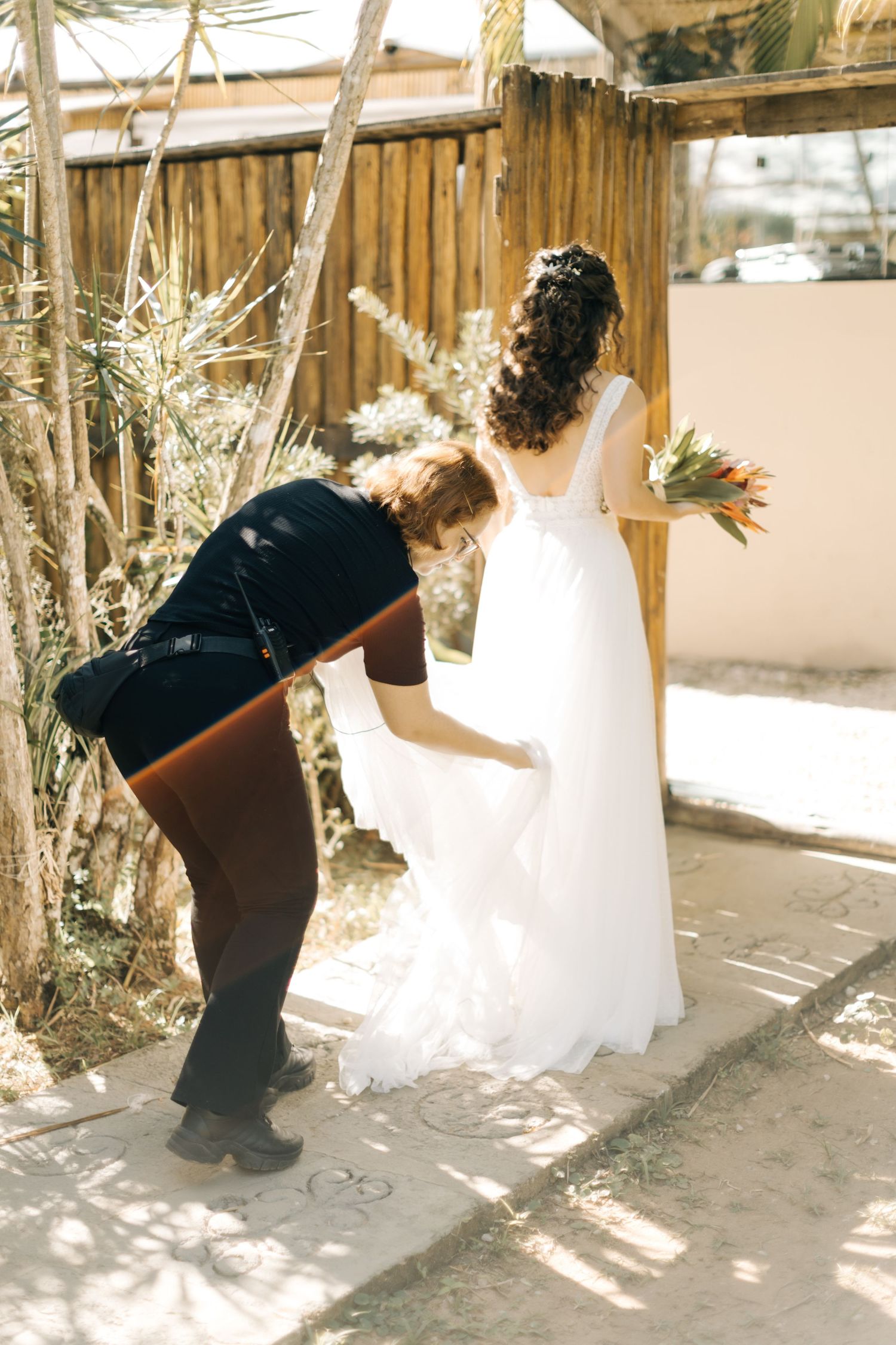 Wedding dress preparation in a rustic wooden venue with dappled sunlight.