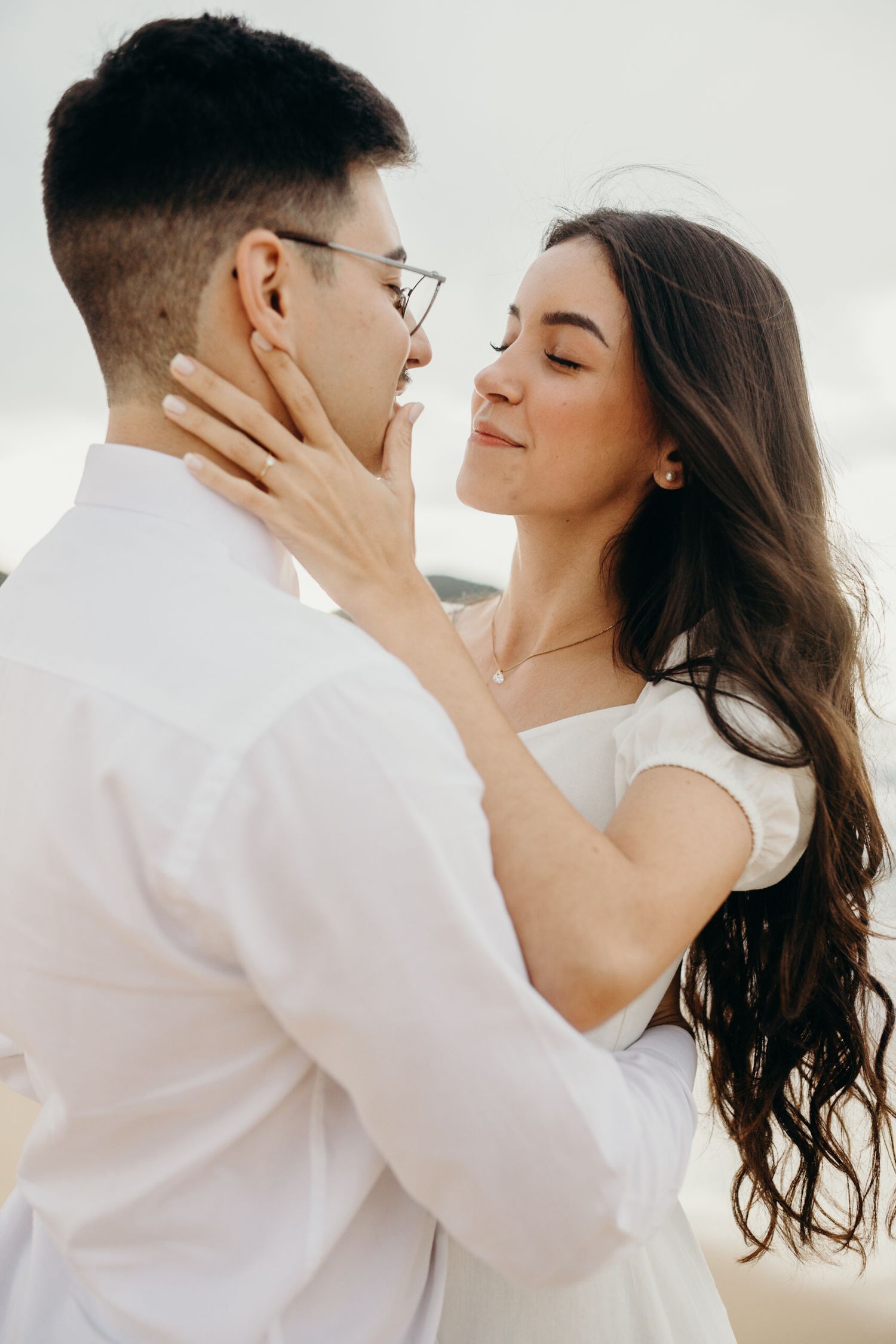 A tender moment between a couple in white clothing against a bright background.