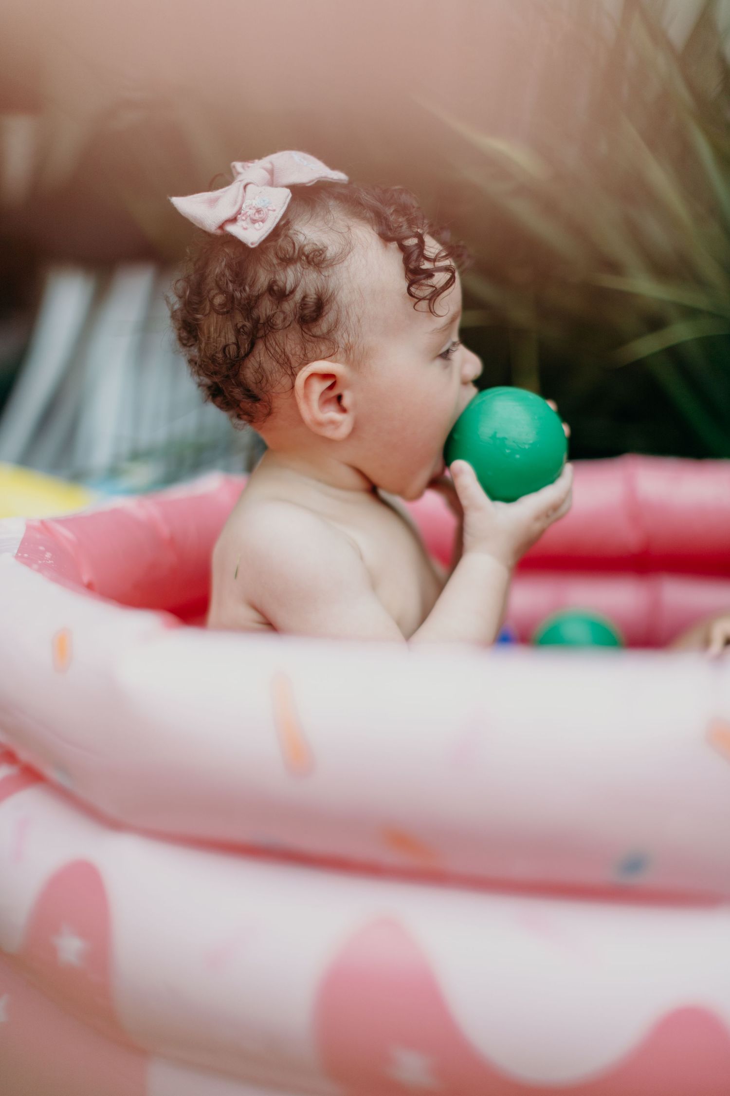 Child playing with colorful balls in a pink and white inflatable pool outdoors.