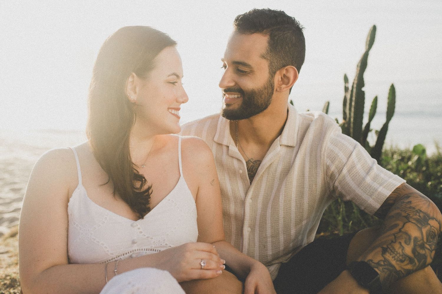 Couple laughing together in natural desert landscape with cactus in background.