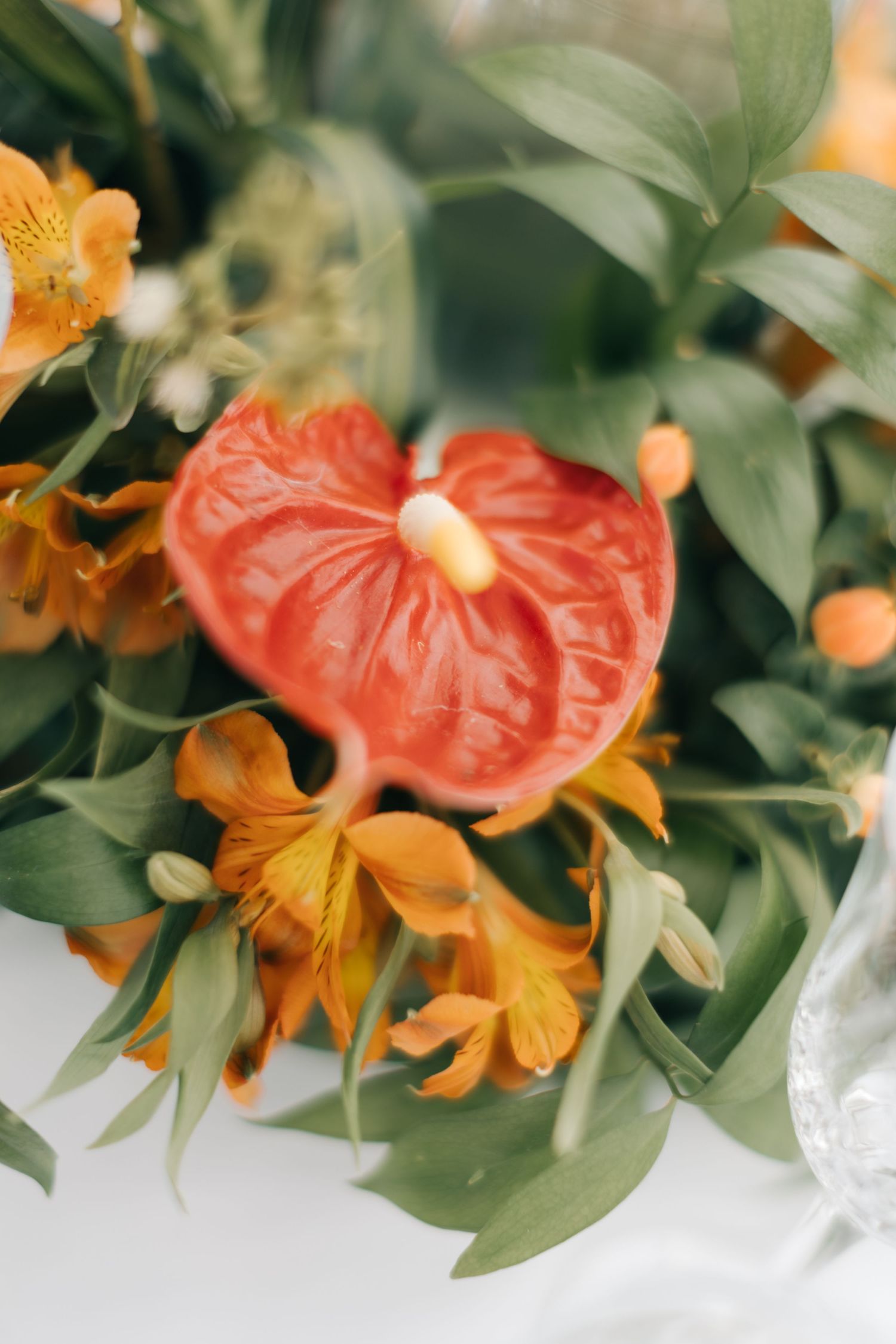 Close-up of tropical floral arrangement with orange lilies and coral anthurium flowers.
