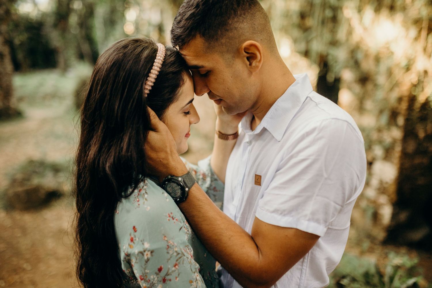 Intimate portrait of couple touching foreheads against natural forest backdrop.