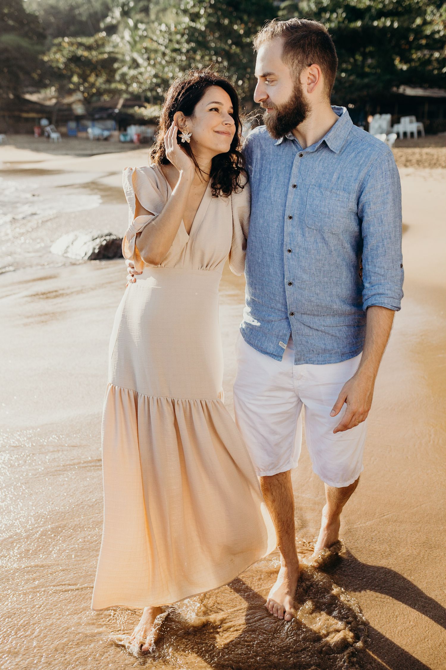A couple shares an intimate moment on a sunny beach while wearing coordinating beige and blue outfits.