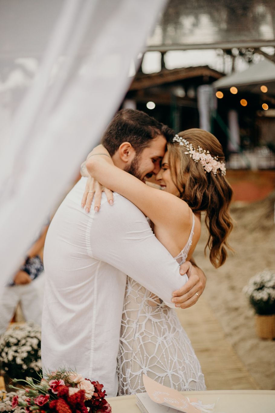 A couple shares an intimate kiss during their beach wedding ceremony while wearing white attire.
