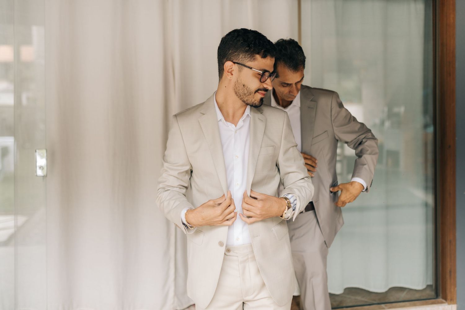 Two people in matching light suits preparing formal attire.