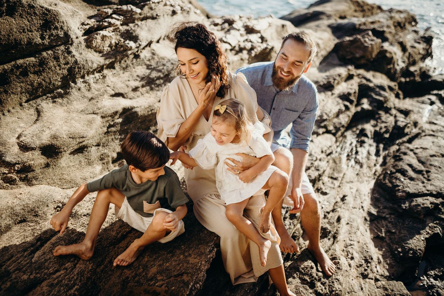 A spontaneous family moment captured on rocky coastal terrain during sunset.
