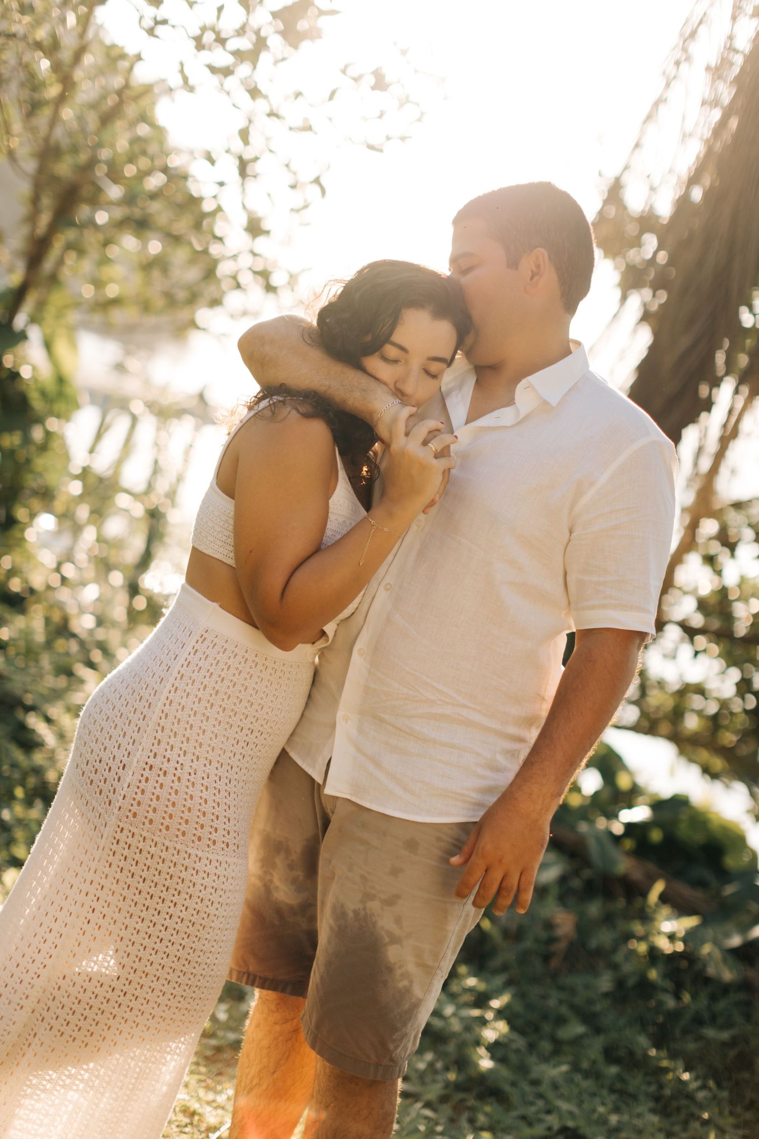 Intimate couple embracing outdoors during sunset with sunlight filtering through trees.