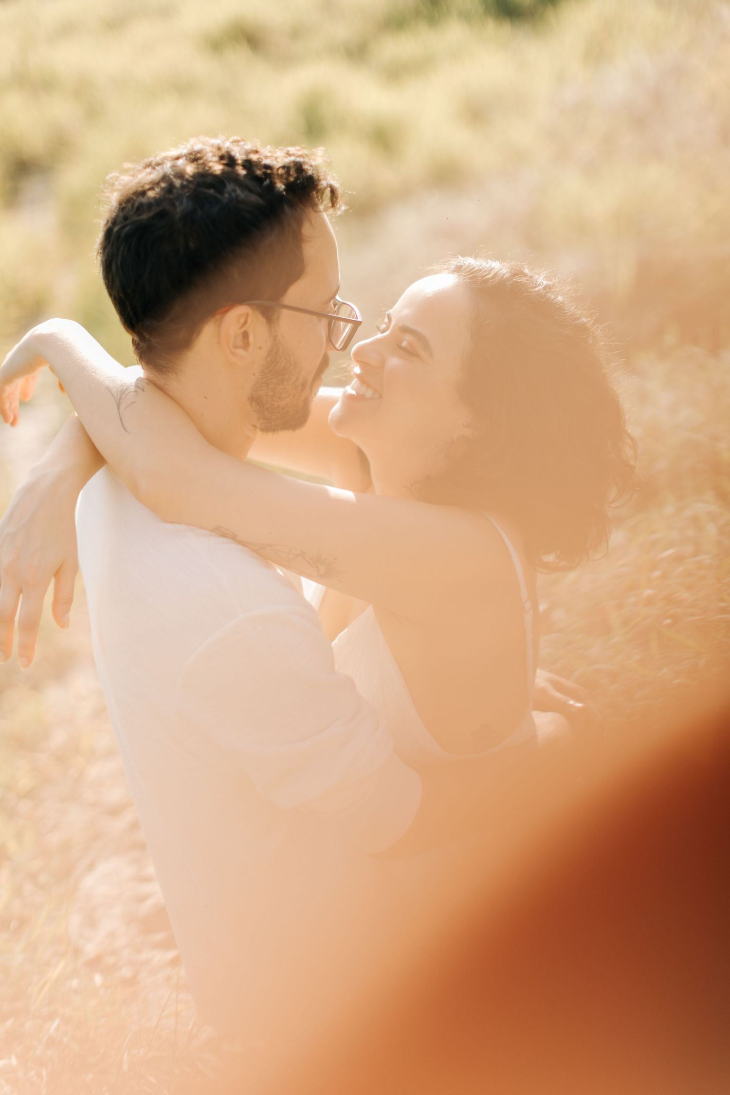Couple embracing in warm sunlight with golden grass in the background.