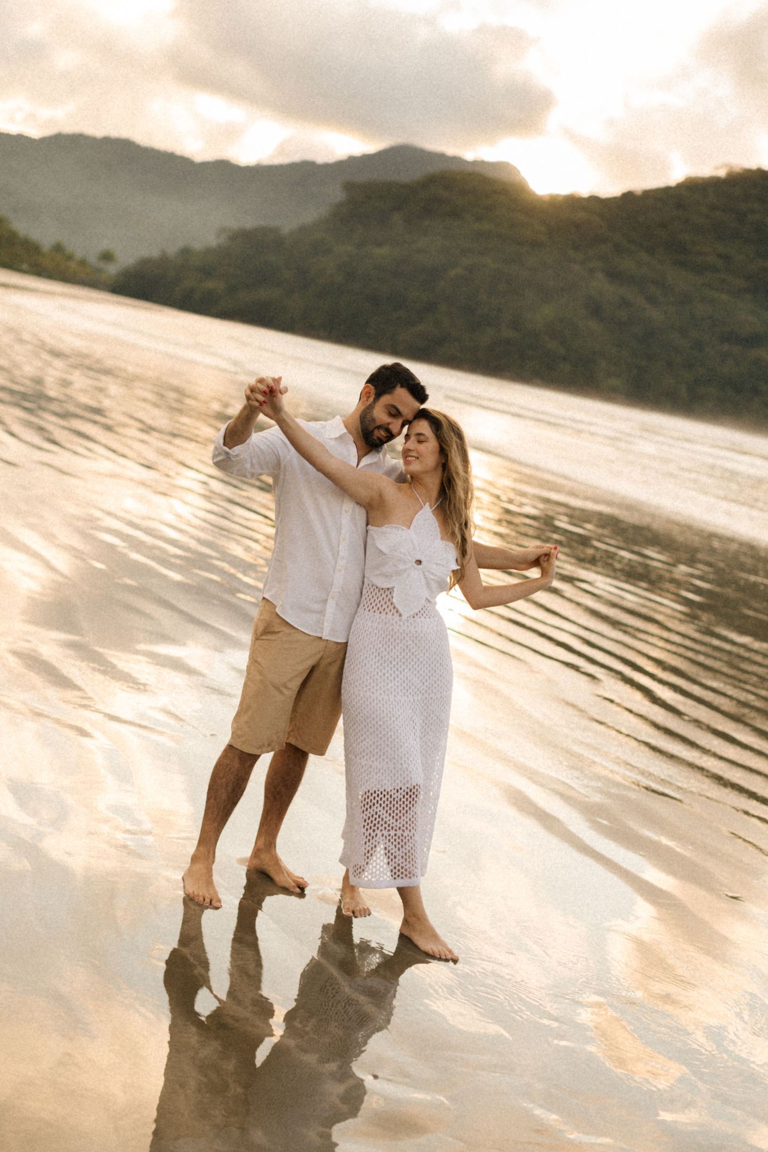 Two people sharing romantic moments while walking barefoot on a misty beach at dusk.