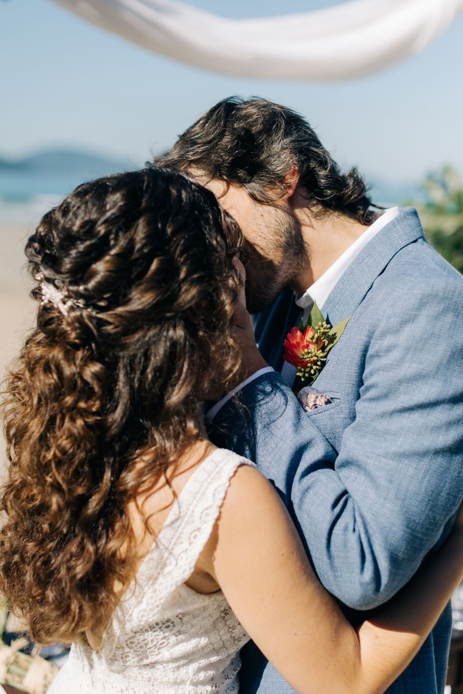 Intimate moment between newlyweds during beach ceremony with ocean backdrop.