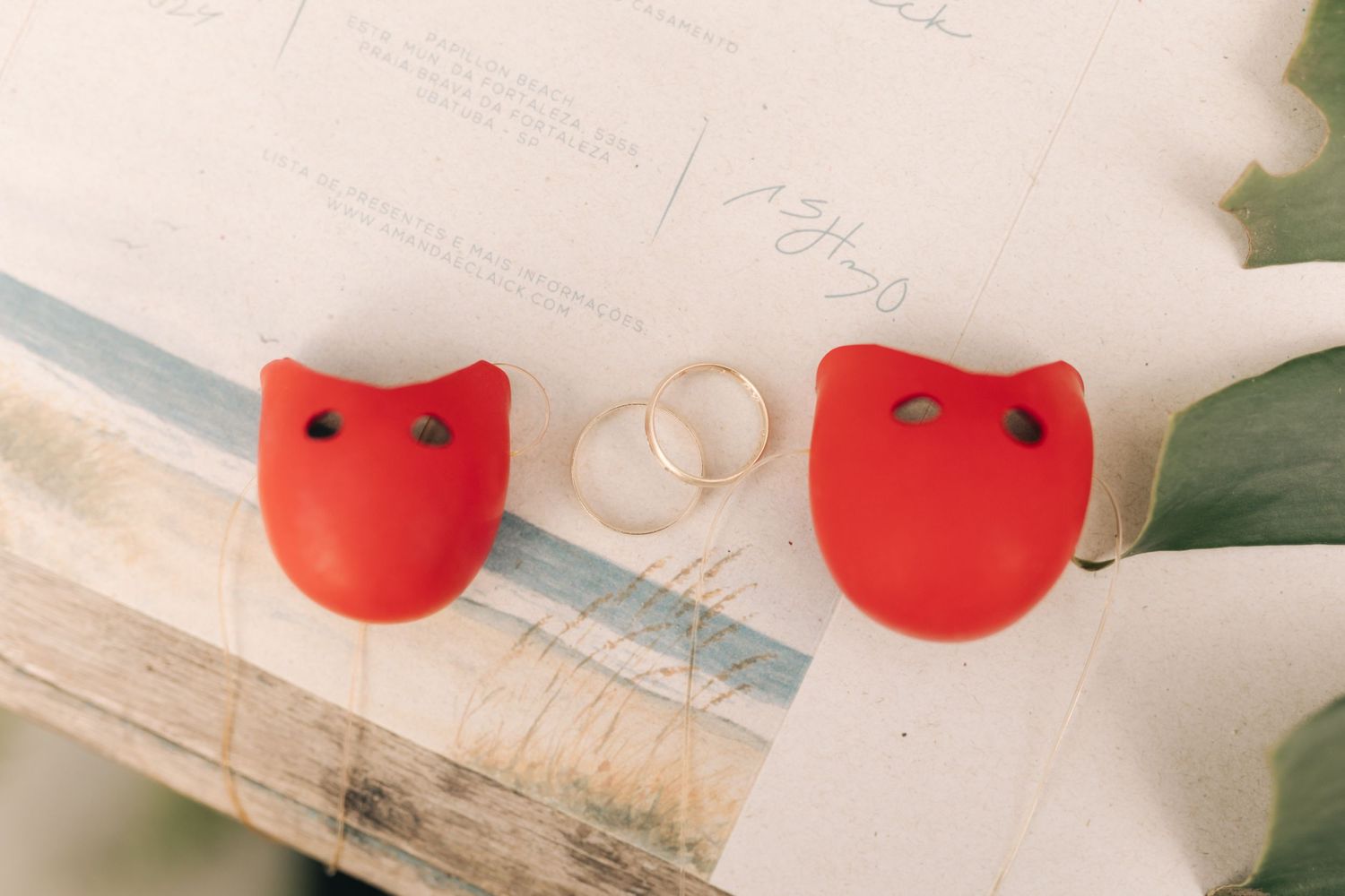 Wedding rings and red decorative elements arranged on white surface.