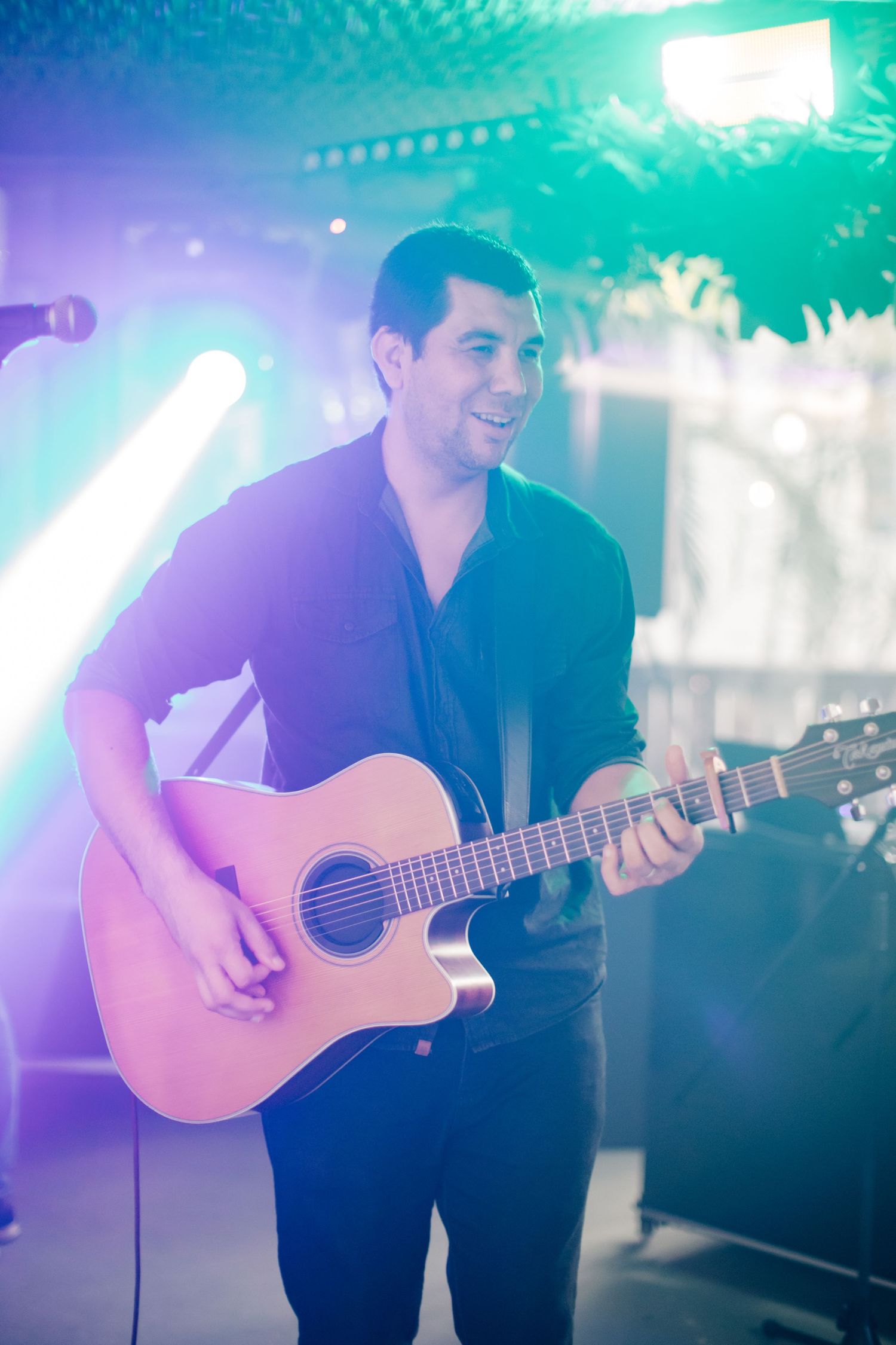 Acoustic guitarist performing under blue and purple stage lights at an indoor venue.