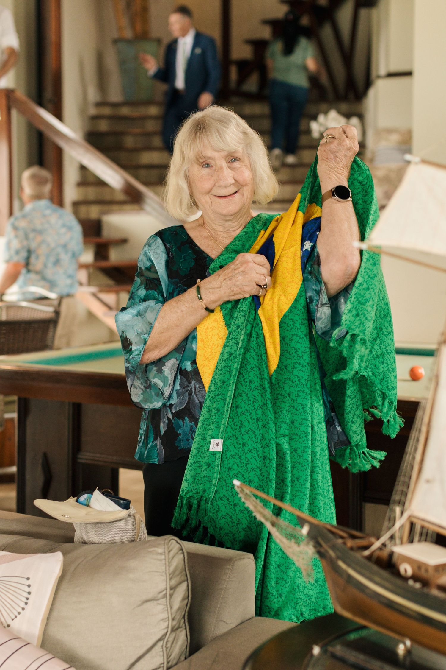 A person in a teal patterned top excitedly holds up a green and yellow Brazilian flag in an indoor setting.