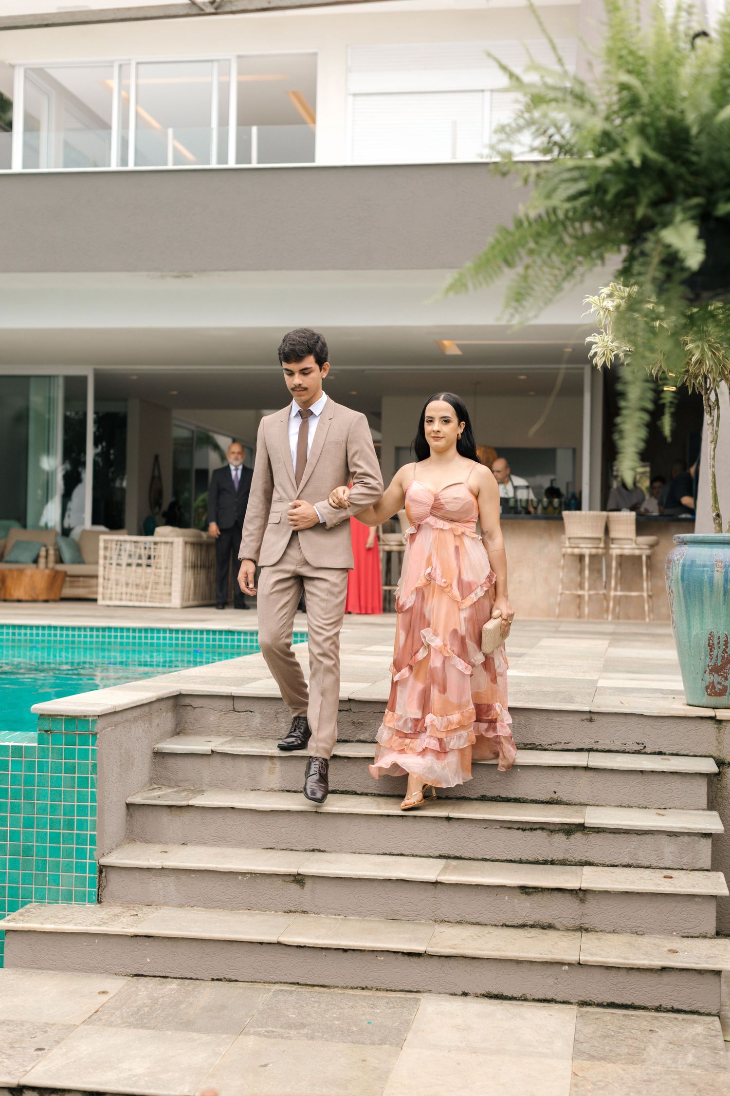 Couple descending pool steps, wearing beige suit and coral floral dress.