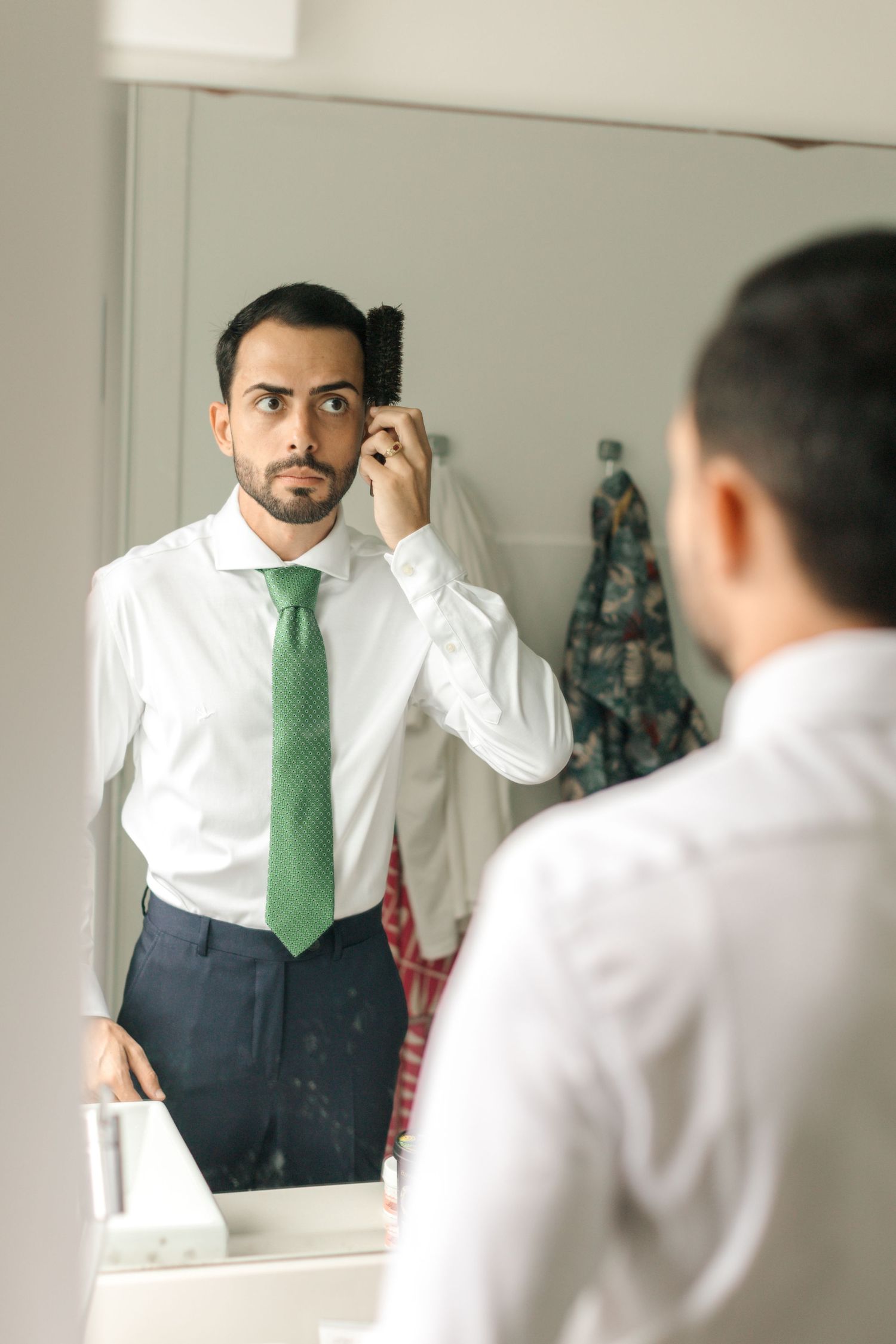 Person in white shirt and green tie adjusting appearance in mirror.