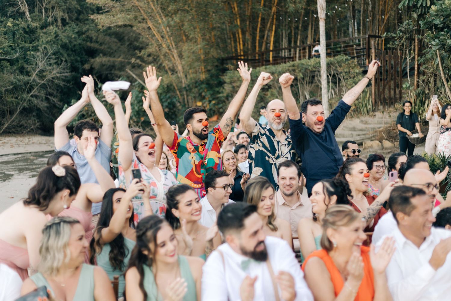 Wedding guests celebrate with raised arms during an outdoor forest ceremony.