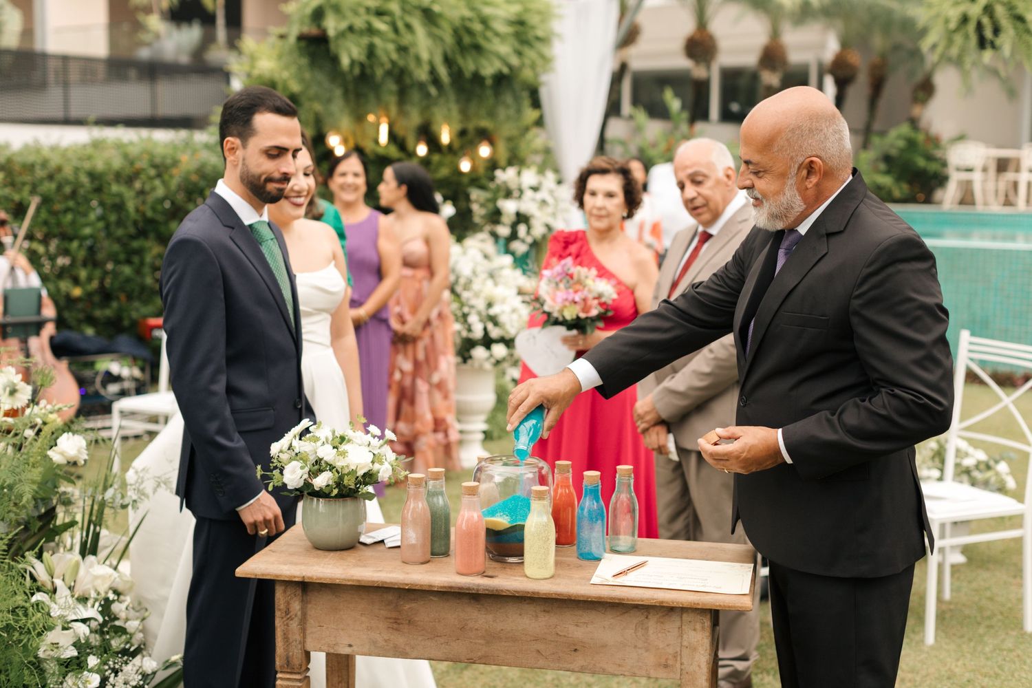 Guests participate in a wedding ceremony ritual with colorful bottled drinks on a wooden table.