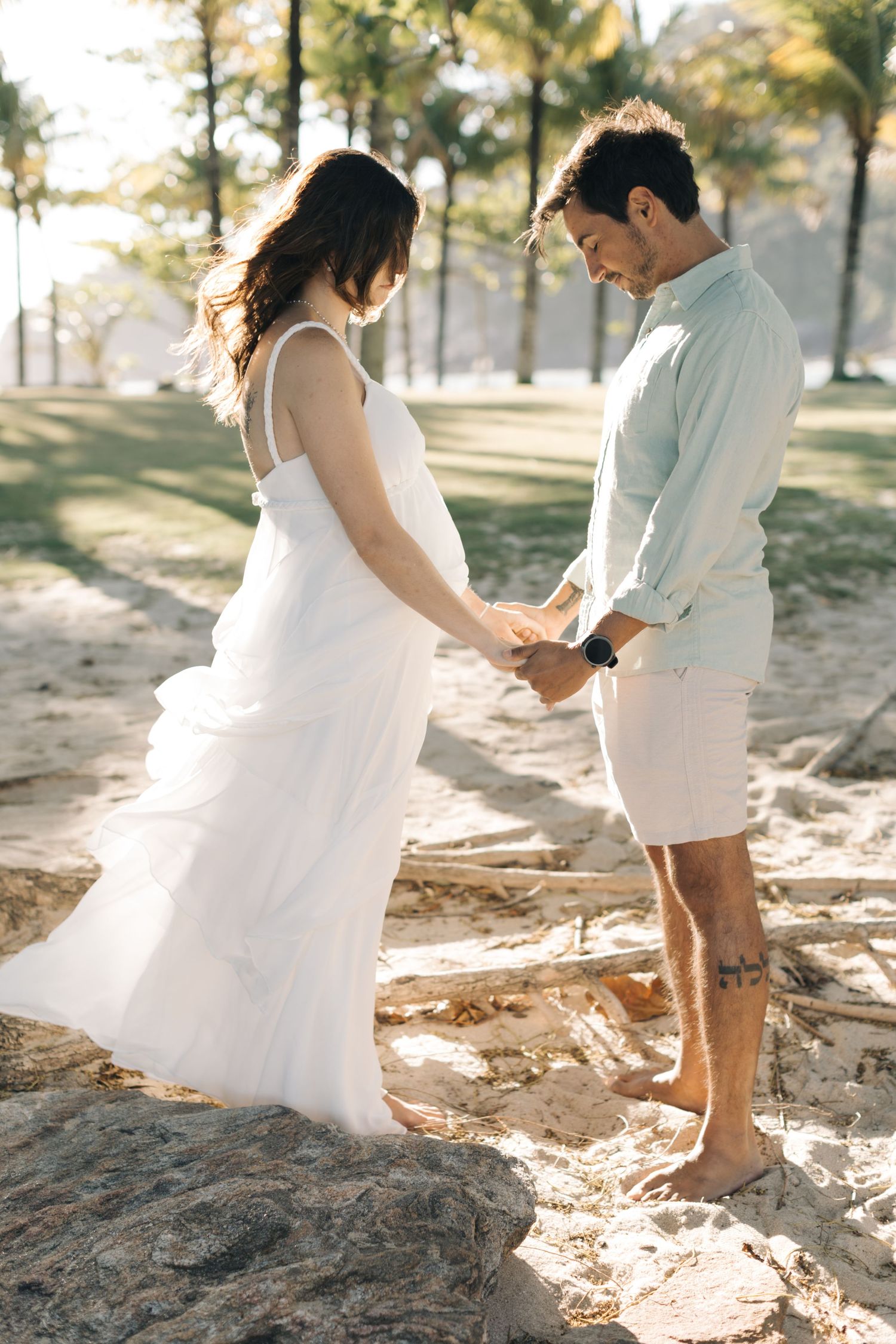 Two people in light colored outfits share a romantic moment on a sunlit beach path.