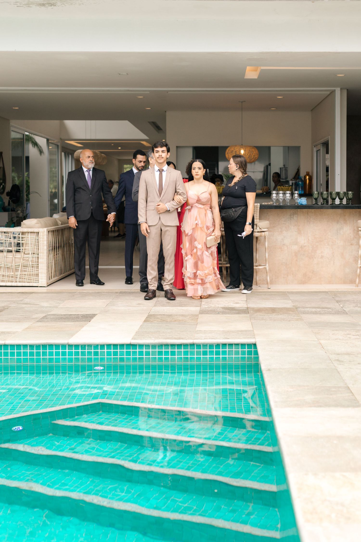 Wedding party gathered by modern poolside with turquoise water.