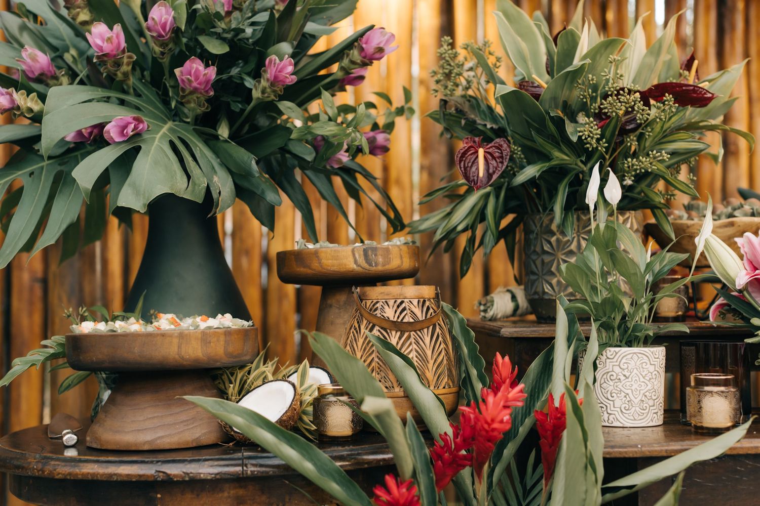 Decorative tropical plant display with pink and red flowers in earthen vessels.