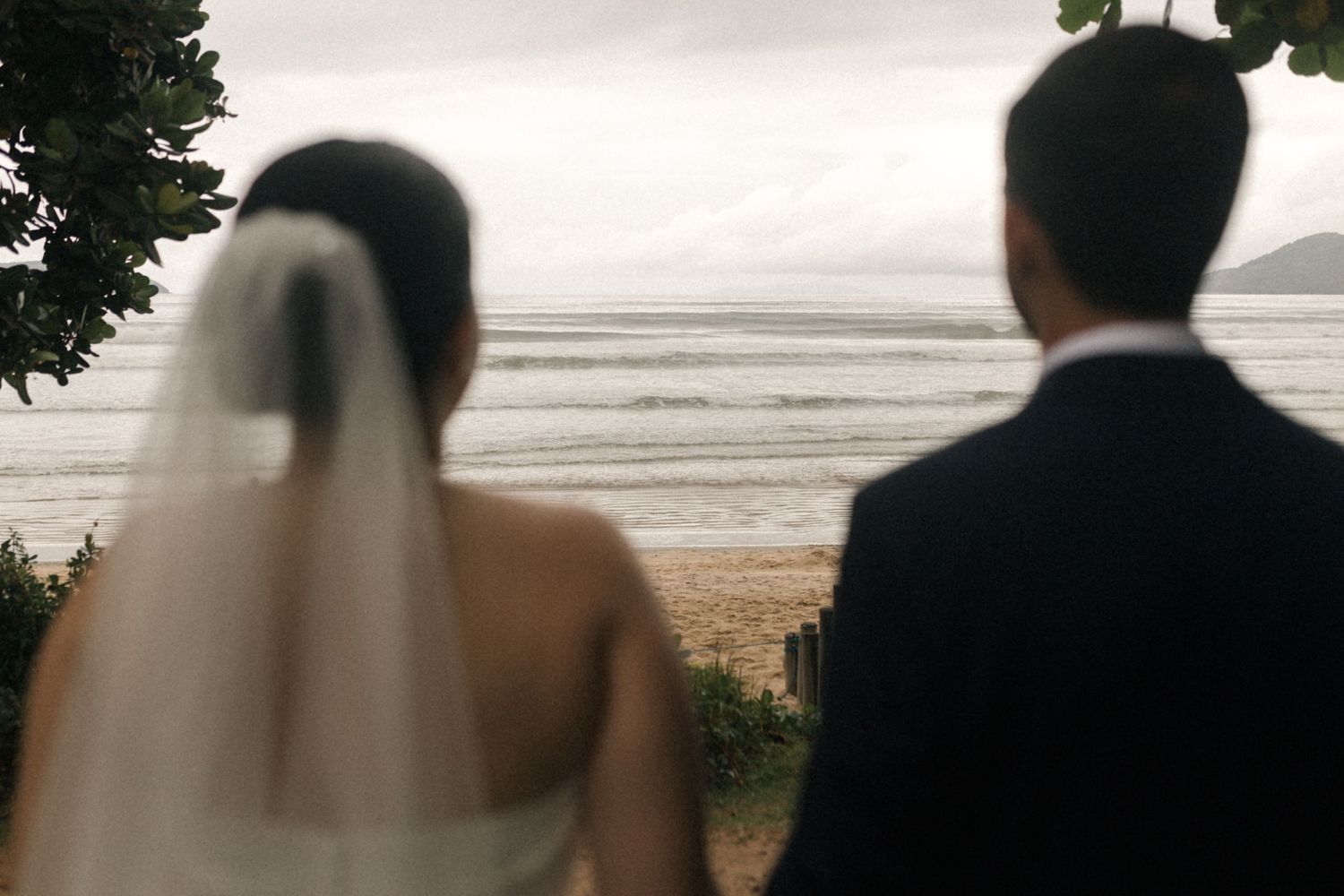 Silhouettes of a wedding couple against an overcast beach backdrop.