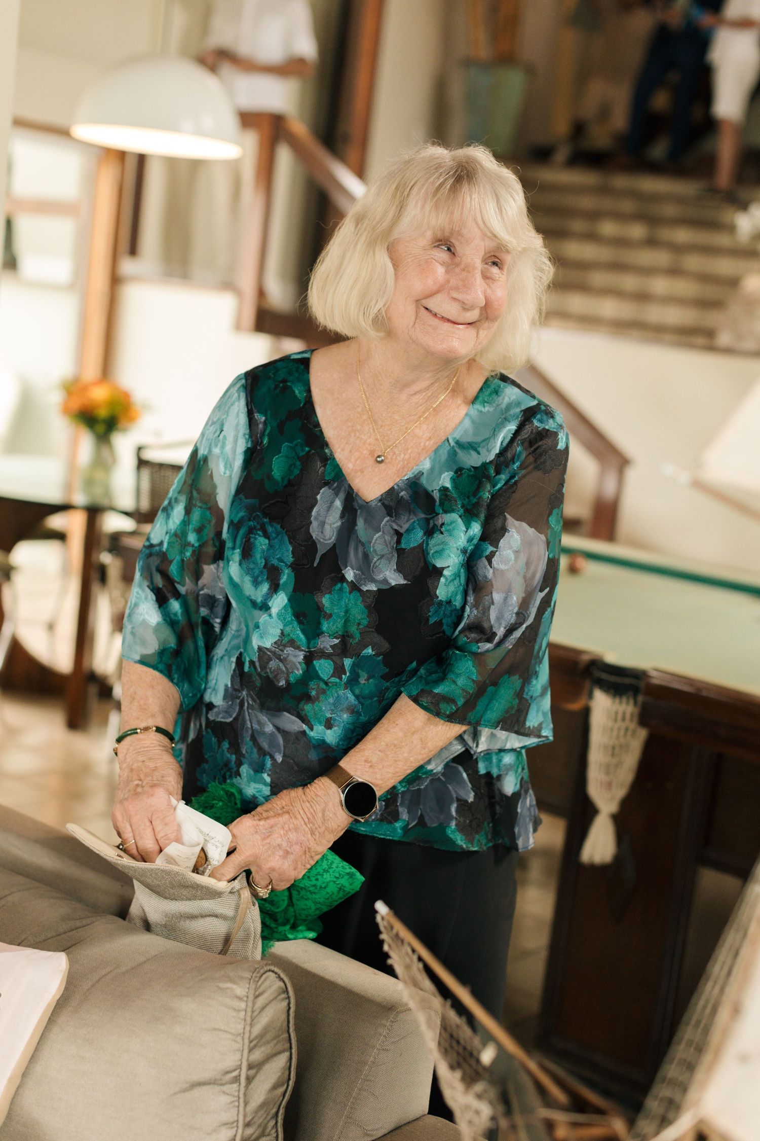 A person wearing a green and black floral top smiles while holding an object in an indoor setting.