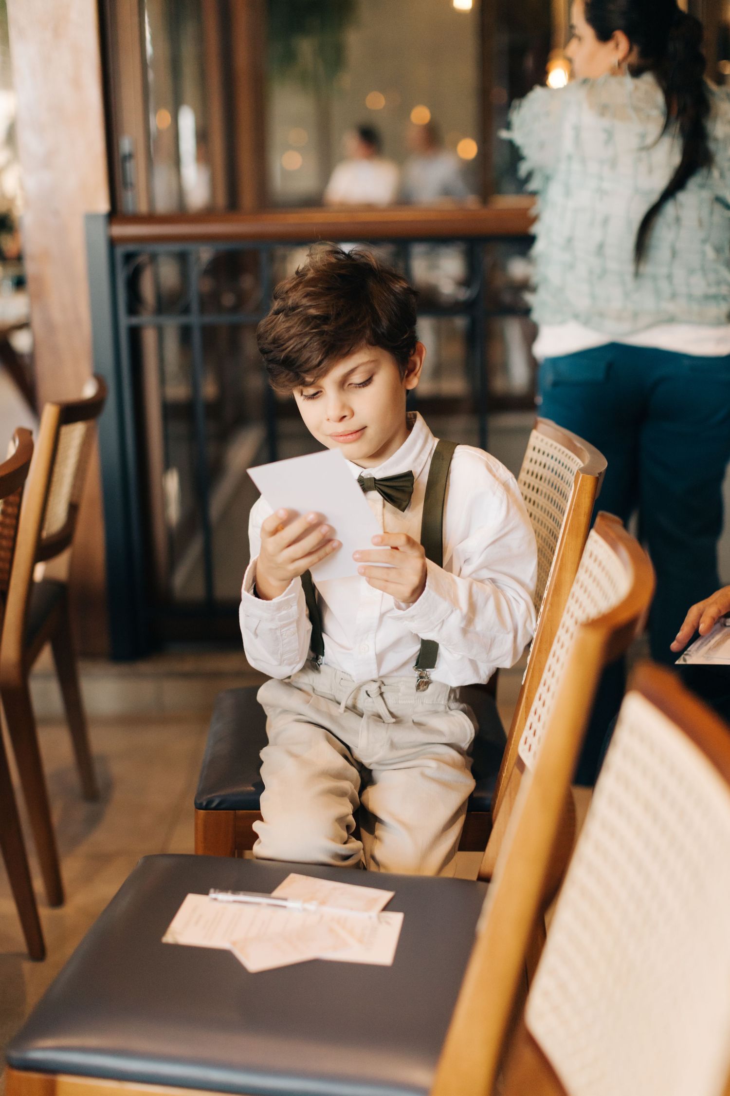 Young attendee in formal wear reads from papers while seated in cane-backed chair.