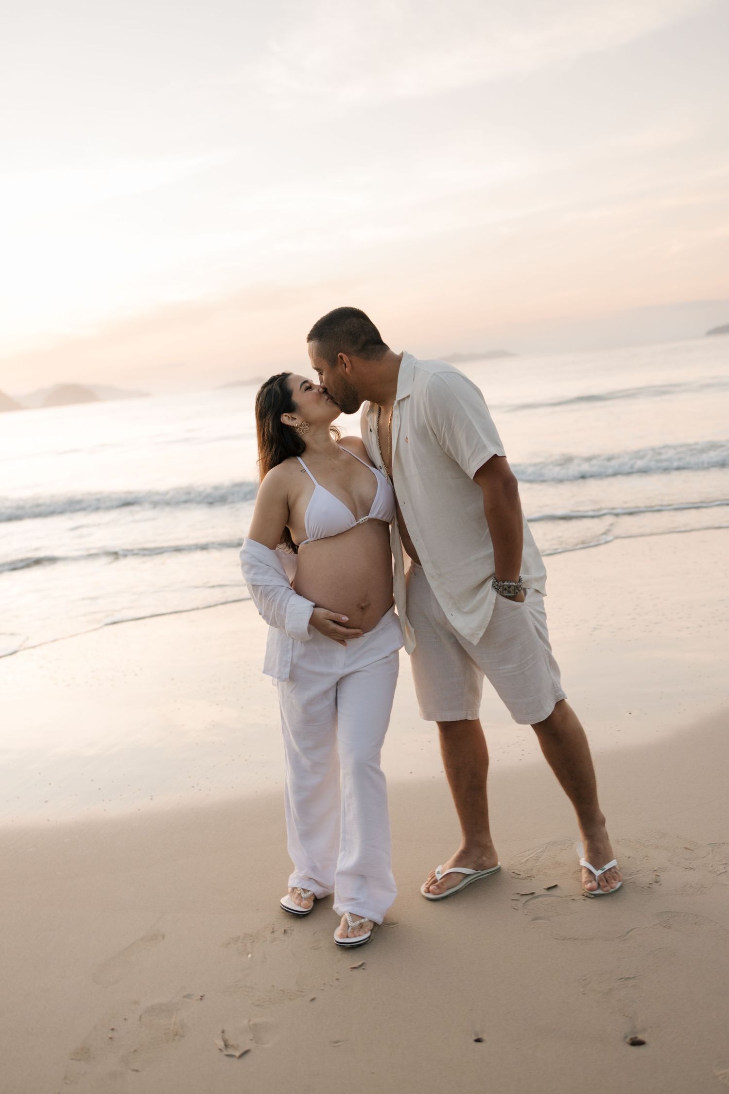 Intimate moment between couple during beachside maternity photoshoot at sunset.