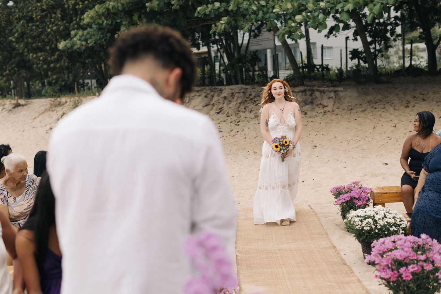 A beachside wedding ceremony with vibrant pink flowers and a bride walking down a sandy aisle.