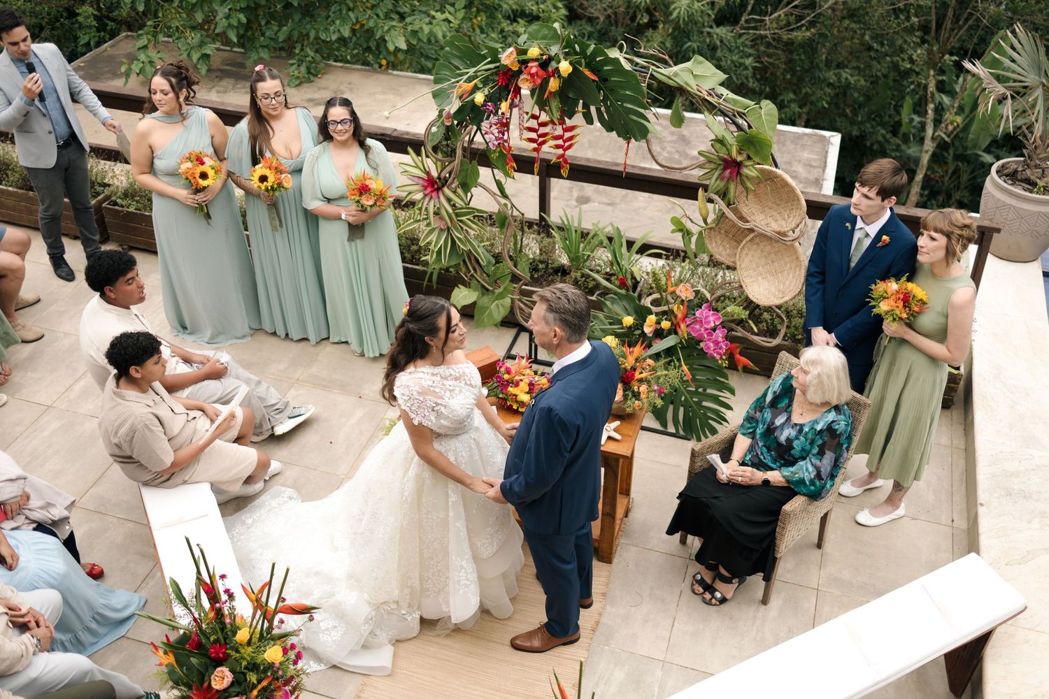 Wedding ceremony guests gather outdoors with tropical decor and mint green bridesmaid dresses.