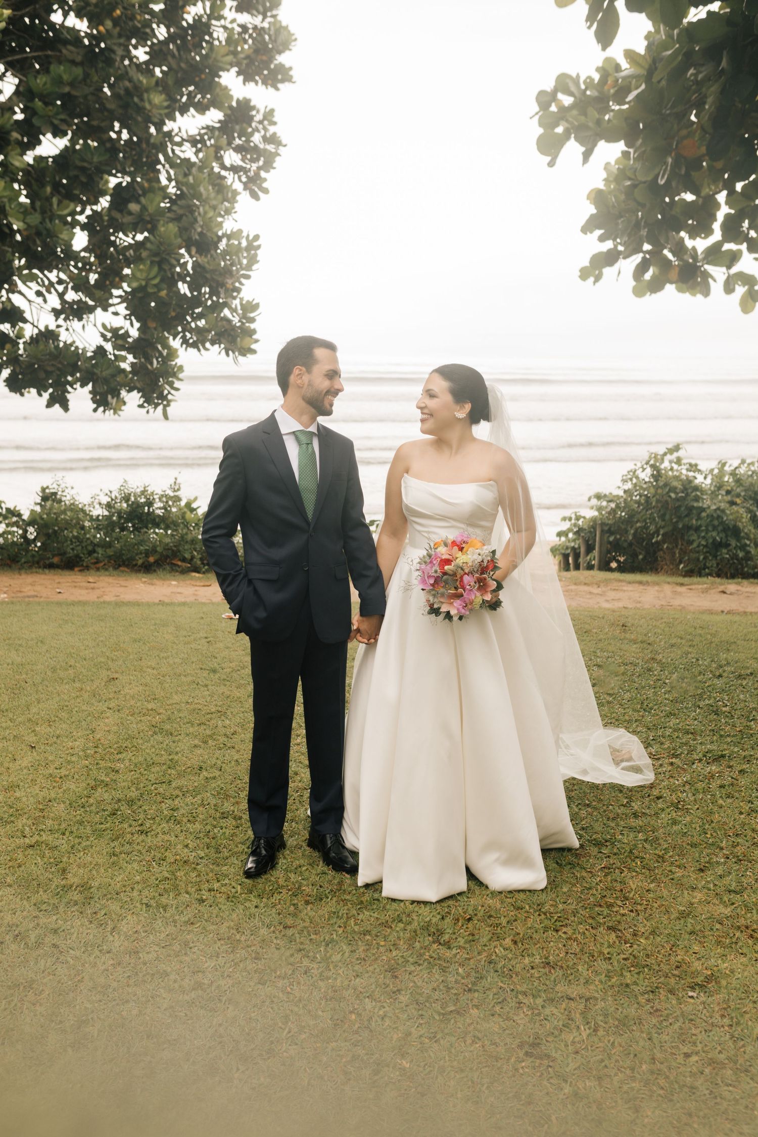 Newlyweds share a joyful moment on their wedding day against an oceanside backdrop.