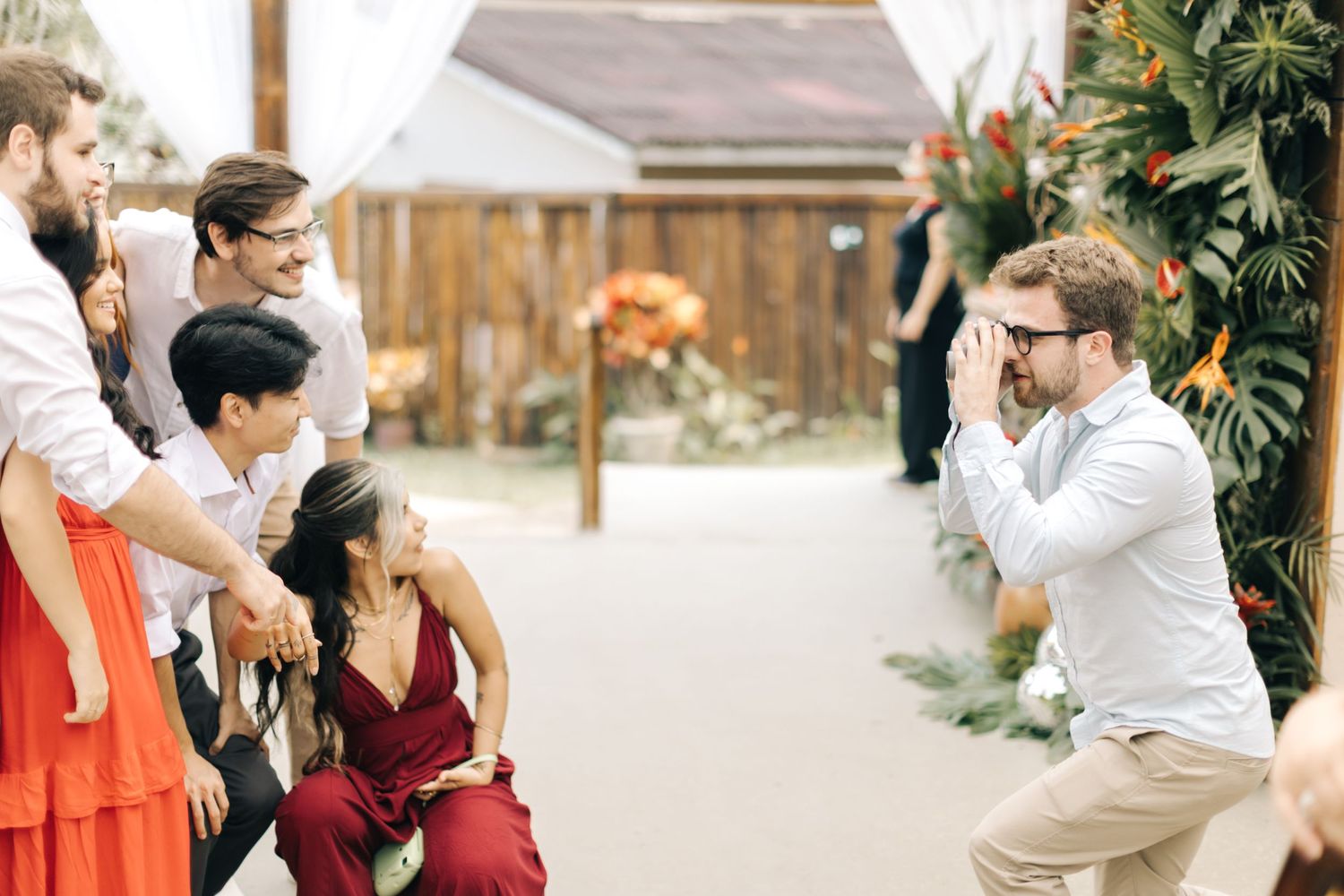 Wedding guests share a playful moment during outdoor reception with photographer in casual attire.