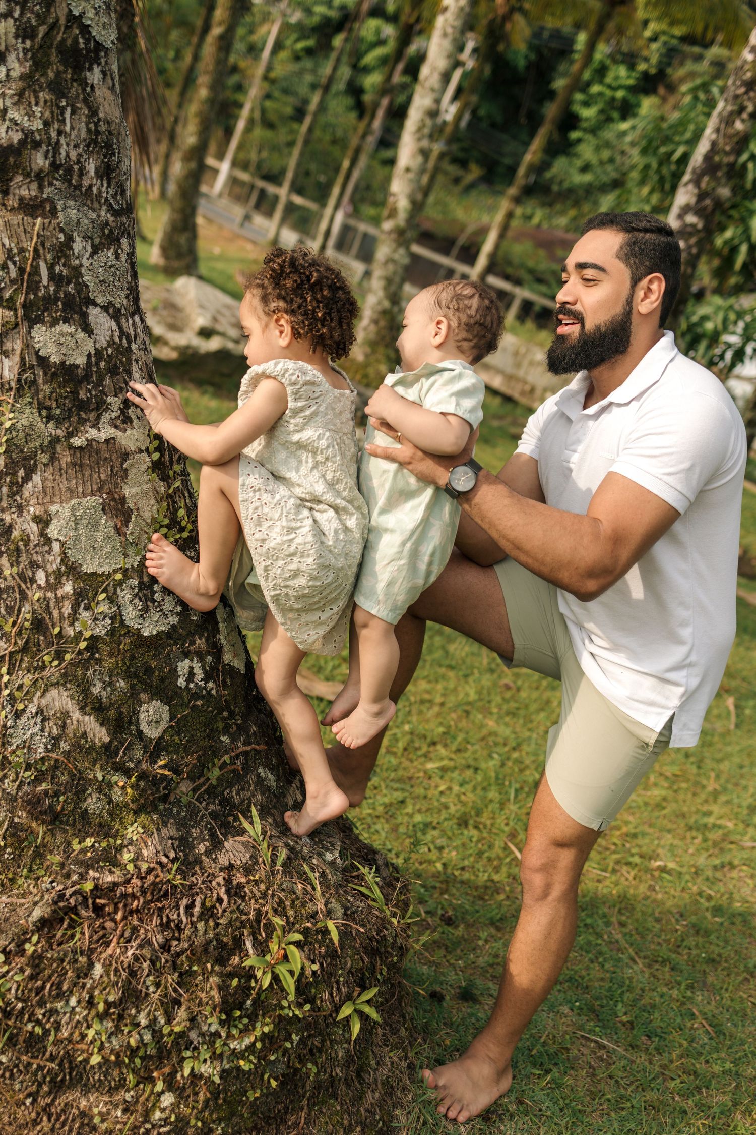 Parent and child playfully climb a tree trunk together in a grassy outdoor setting.