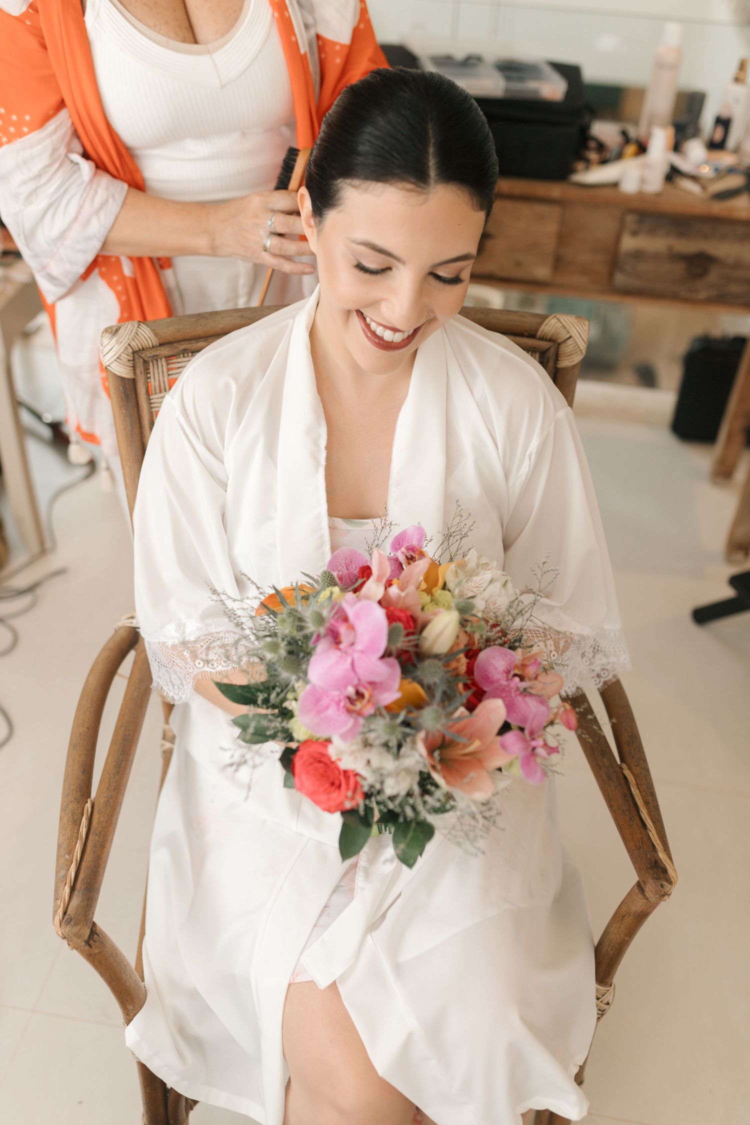 Beautiful bridal bouquet with pink and coral flowers held by someone in white robe.