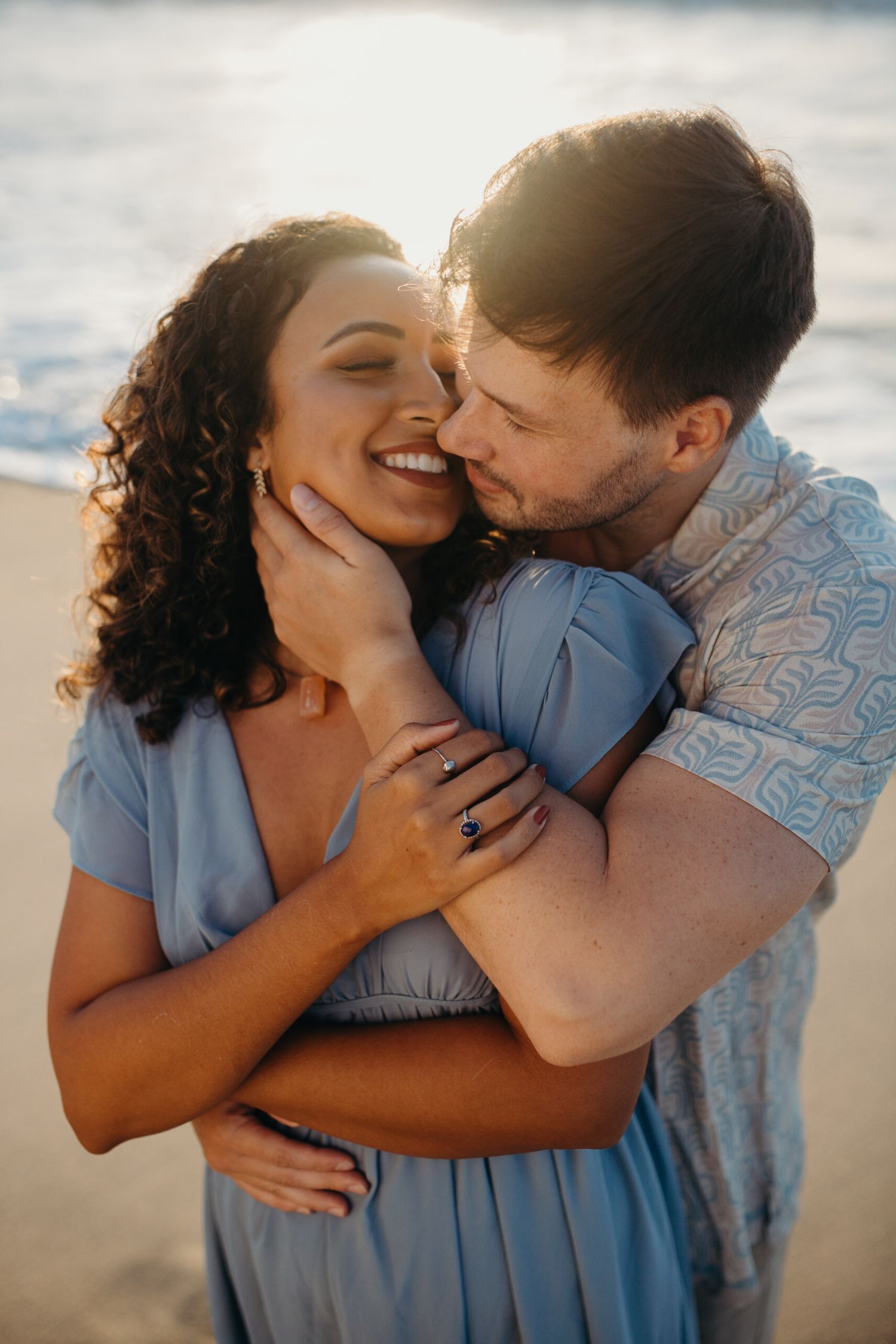 Intimate couple sharing tender moment on sandy beach during golden hour.