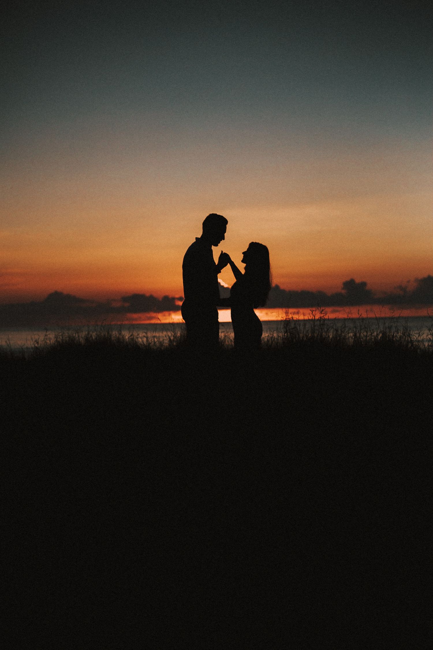 Silhouetted couple standing against dramatic sunset sky over ocean horizon.