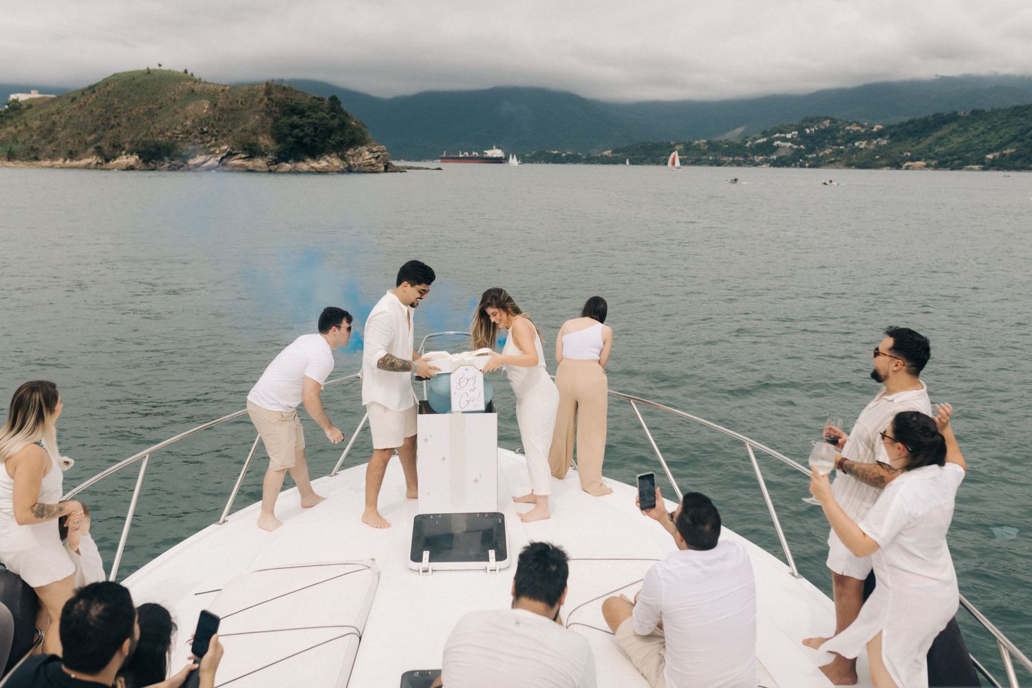 Yacht passengers lounging on white deck with scenic mountain harbor views.