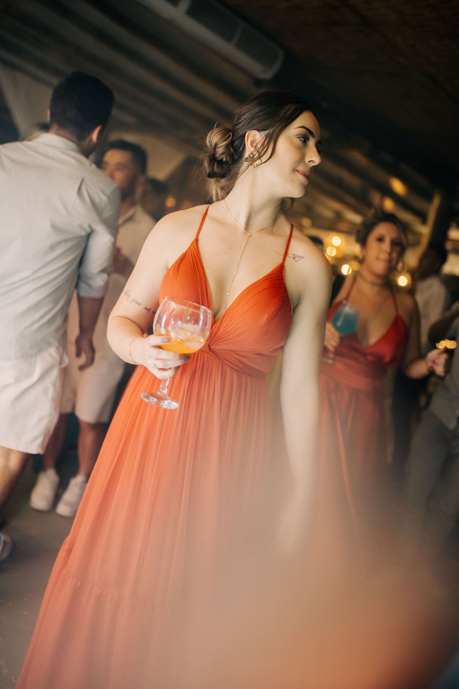Guests in coral bridesmaid dresses dancing at an indoor wedding reception.