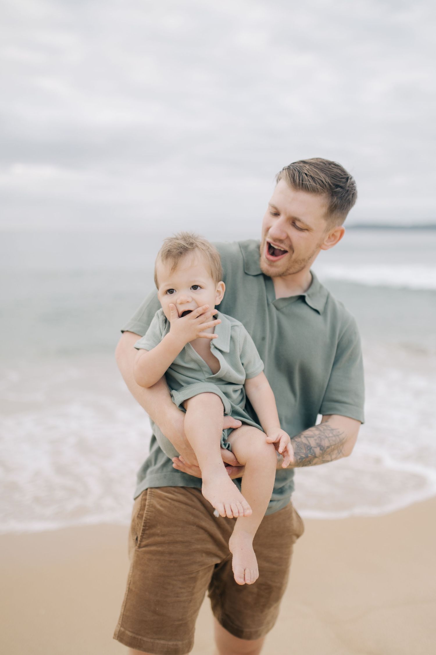 A parent and toddler share genuine laughter during a beach portrait session.